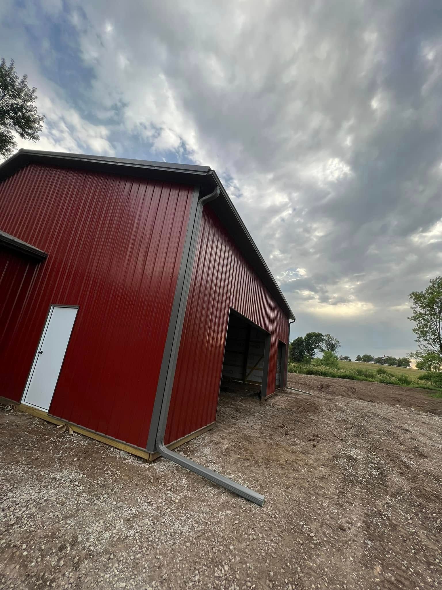 Red barn with striped awning on a gravel lot under a cloudy sky