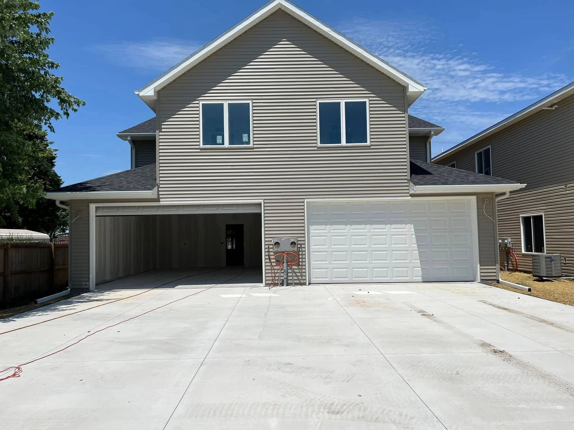 Front view of a two-story house with a large driveway and two-car garage under a clear blue sky