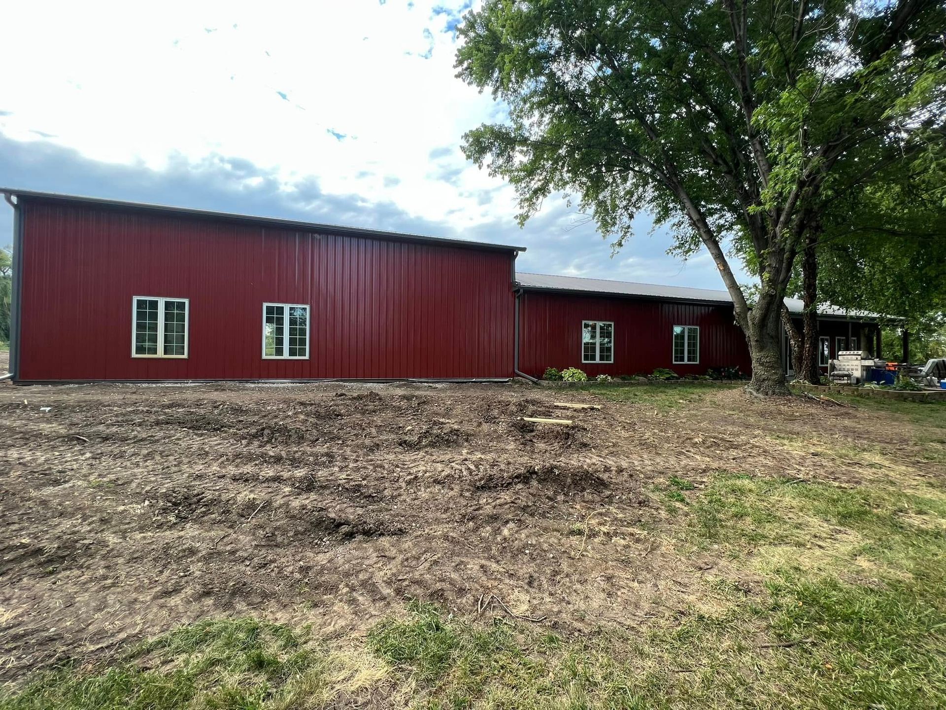 Red barn-style building with white-trimmed windows on a dirt lot, framed by trees under a cloudy sky