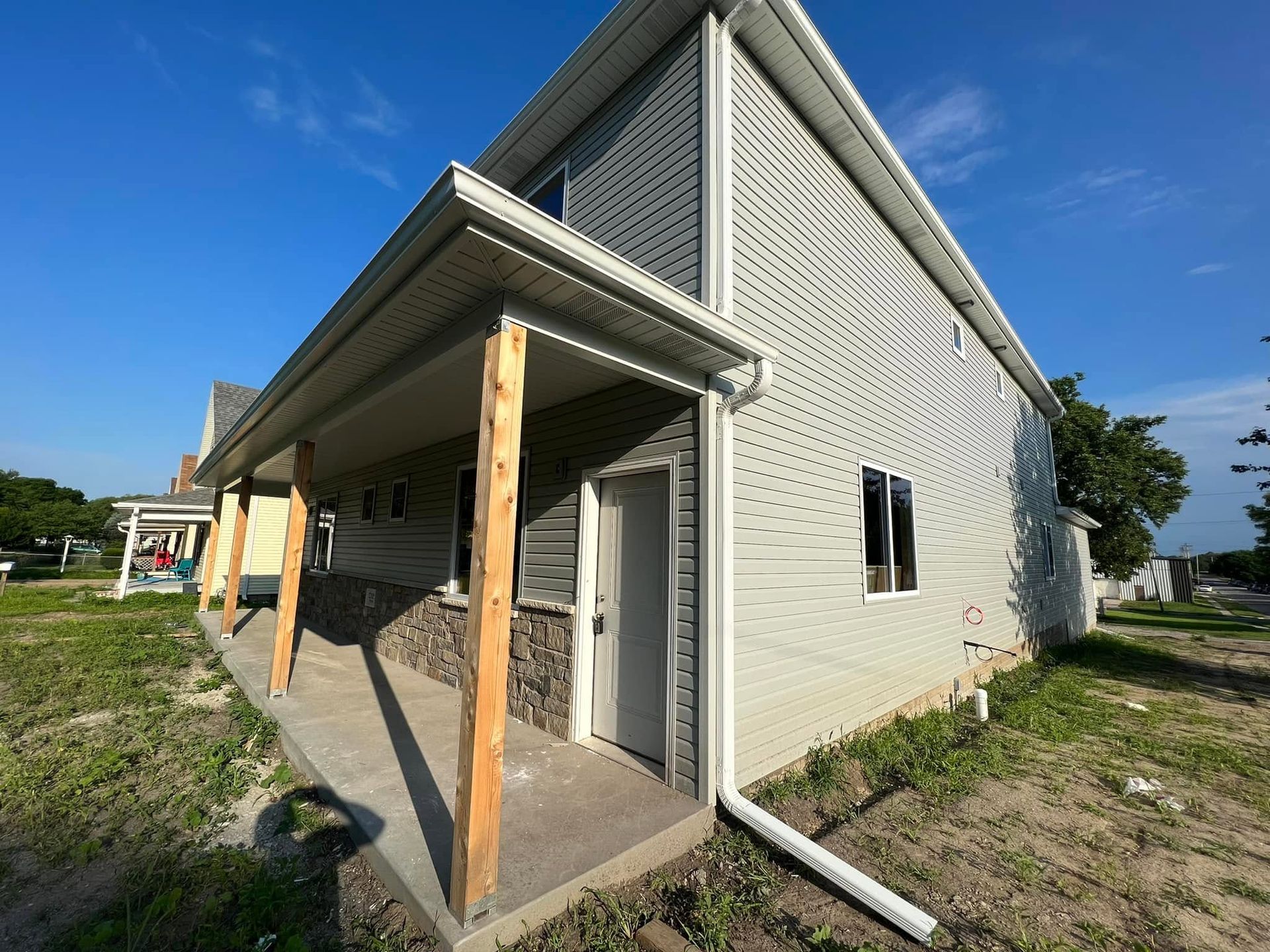 Exterior view of a small unfinished house with light siding, porch posts, and a blue sky background