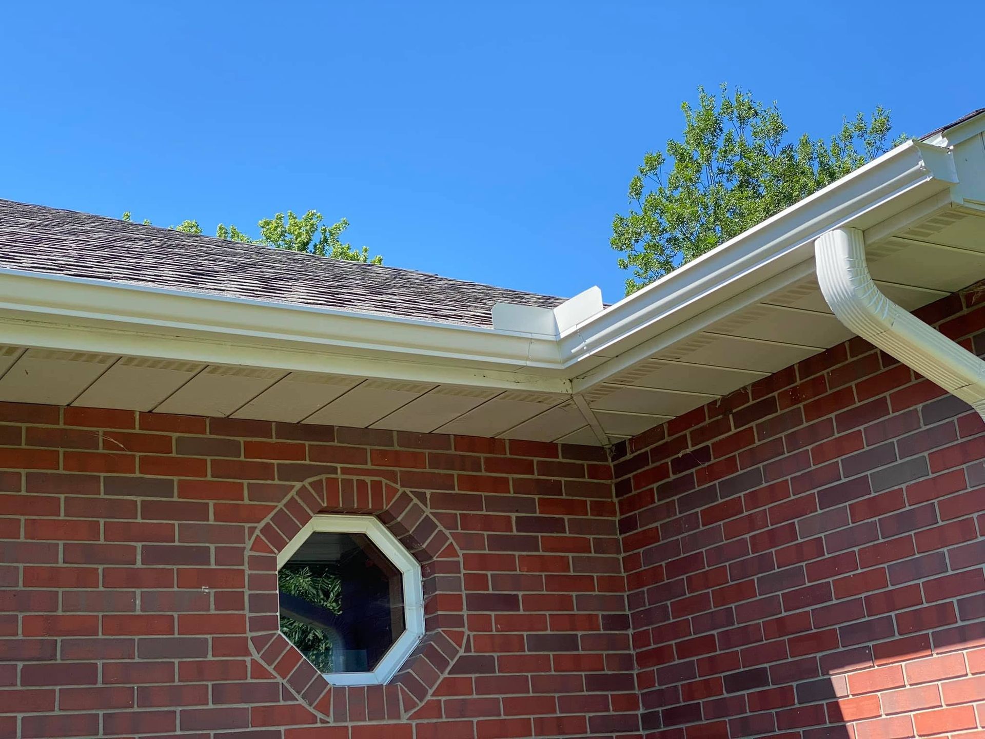 Brick house corner with octagonal window, white gutter, and blue sky above roofline