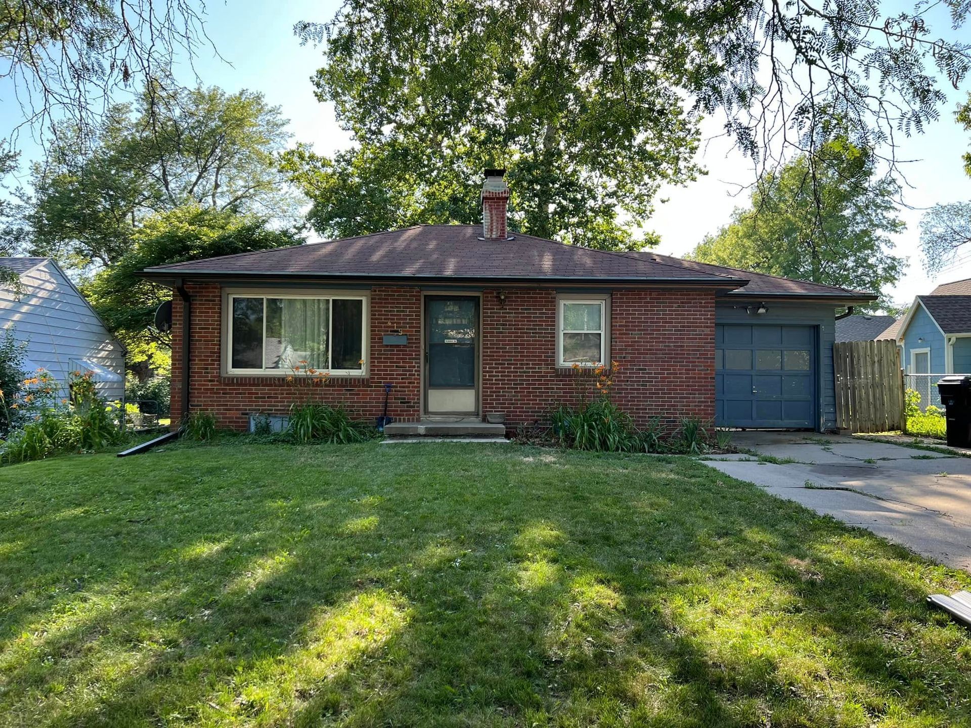 Brick ranch house with blue garage and sunlit front lawn, viewed from the street