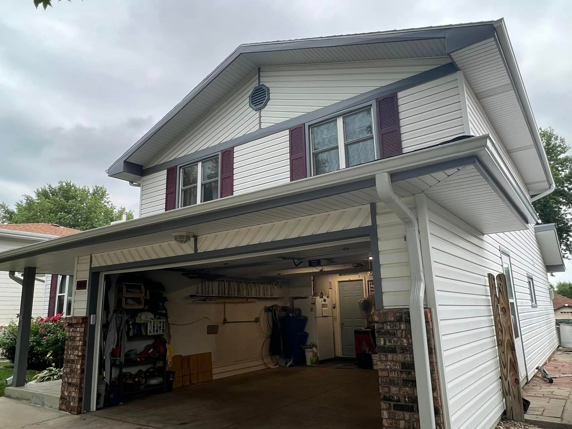 Two-story house with open garage and white siding on a cloudy day