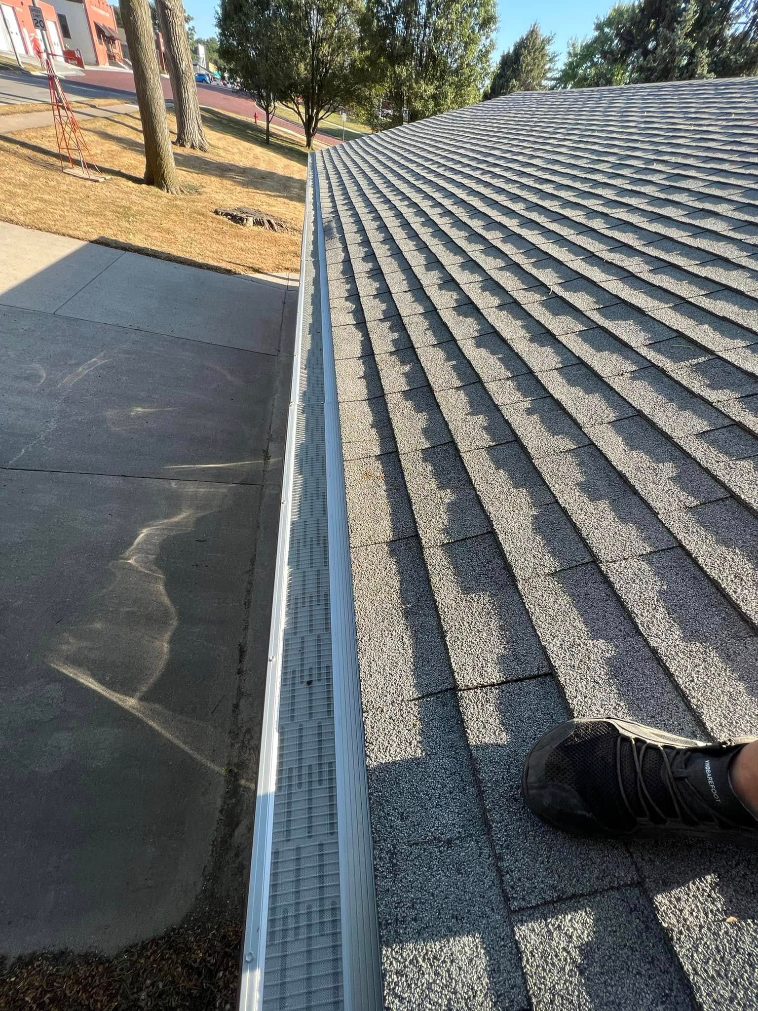 Roof shingles beside a flat roof, with trees and dry ground in the background