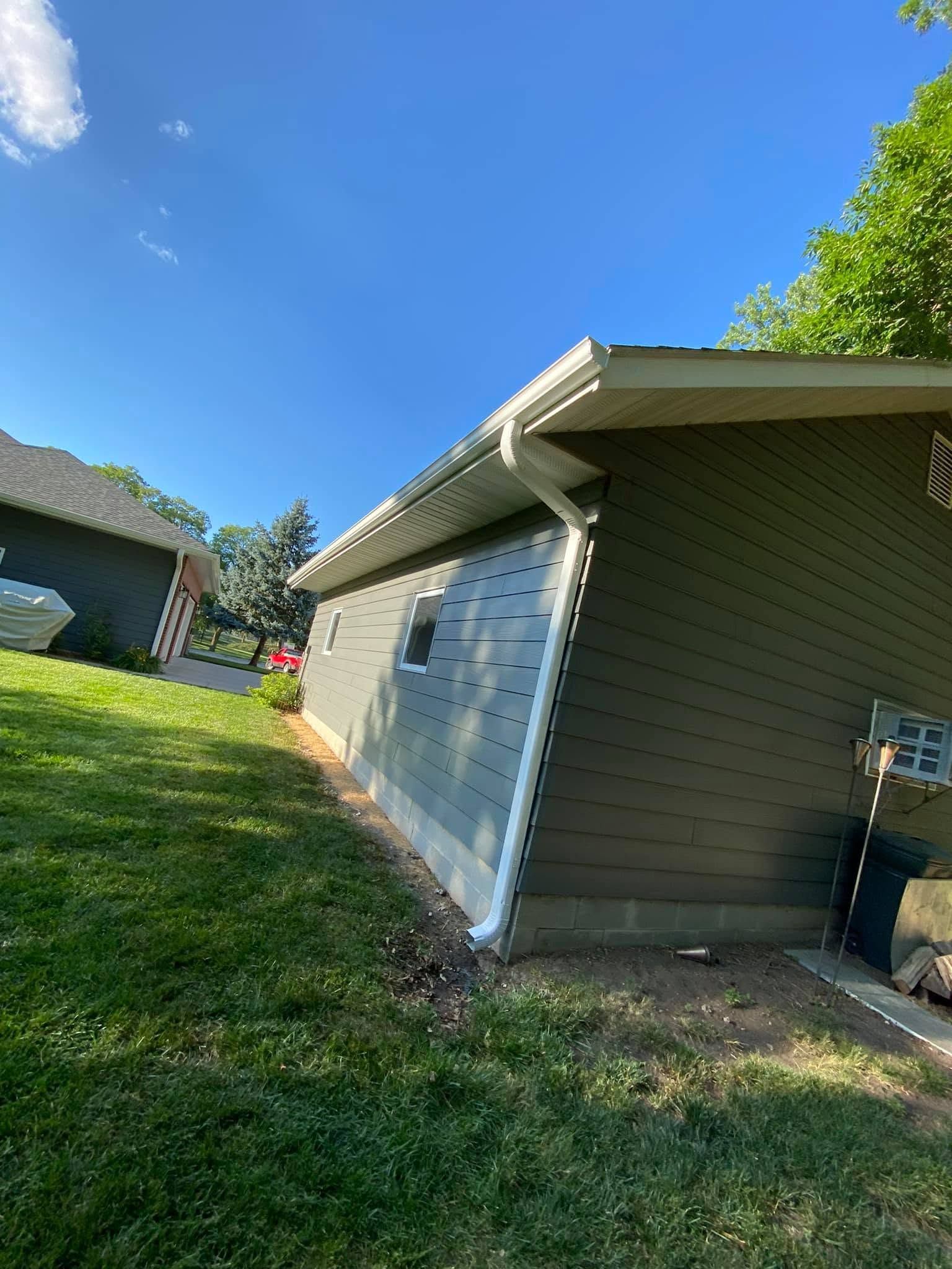 Single-story garage with white doors and beige siding beside a grassy yard under a blue sky.