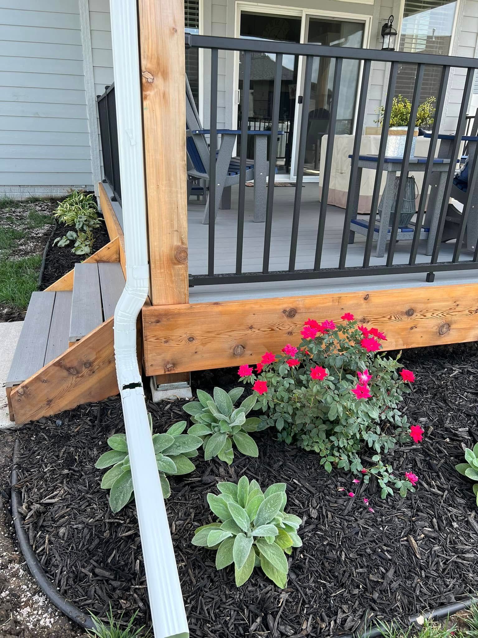 Broken porch railing beside black metal gate and pink flowers with a loose white strip hanging down