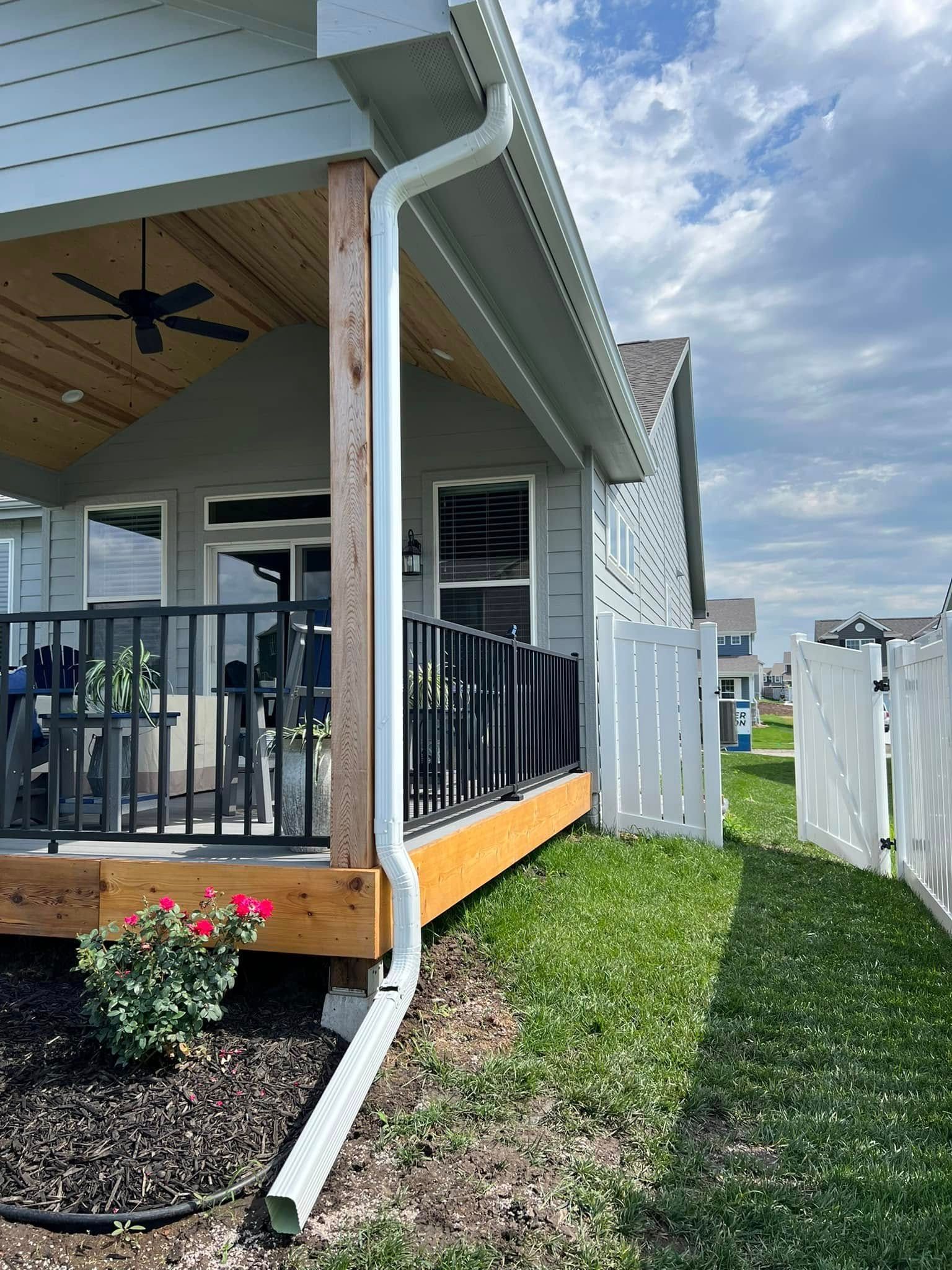 Covered porch with black railing, white siding, and a side yard fence under cloudy skies.