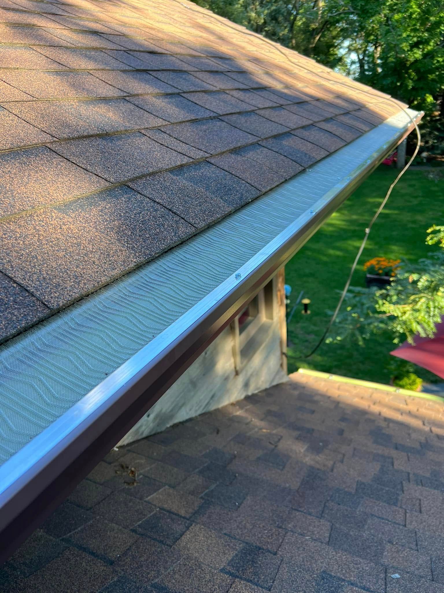 Roof shingles and gutter edge on a house, with trees and lawn in the background