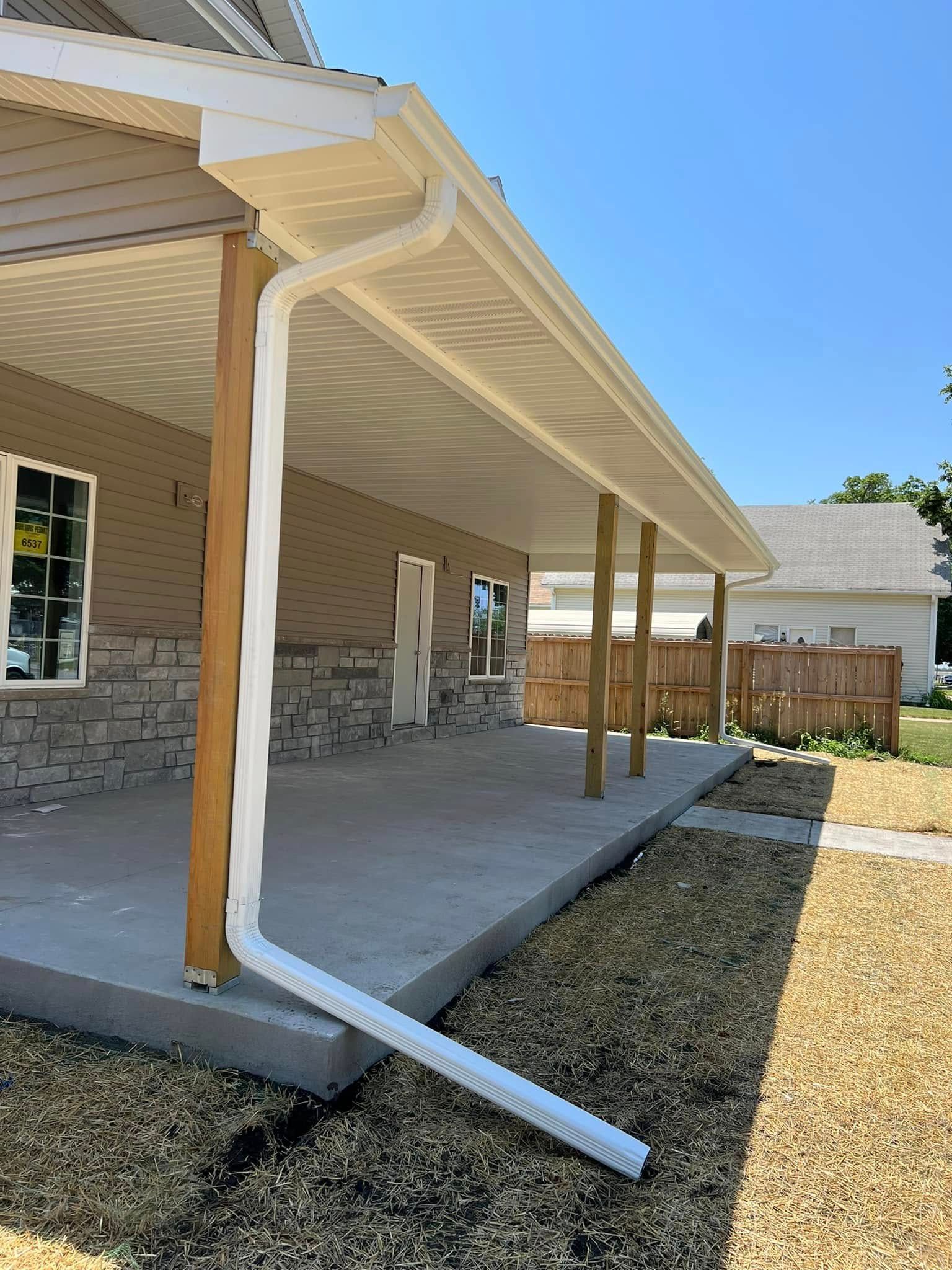 Covered backyard patio with stone walls, white gutters, and a downspout extending onto the concrete slab.
