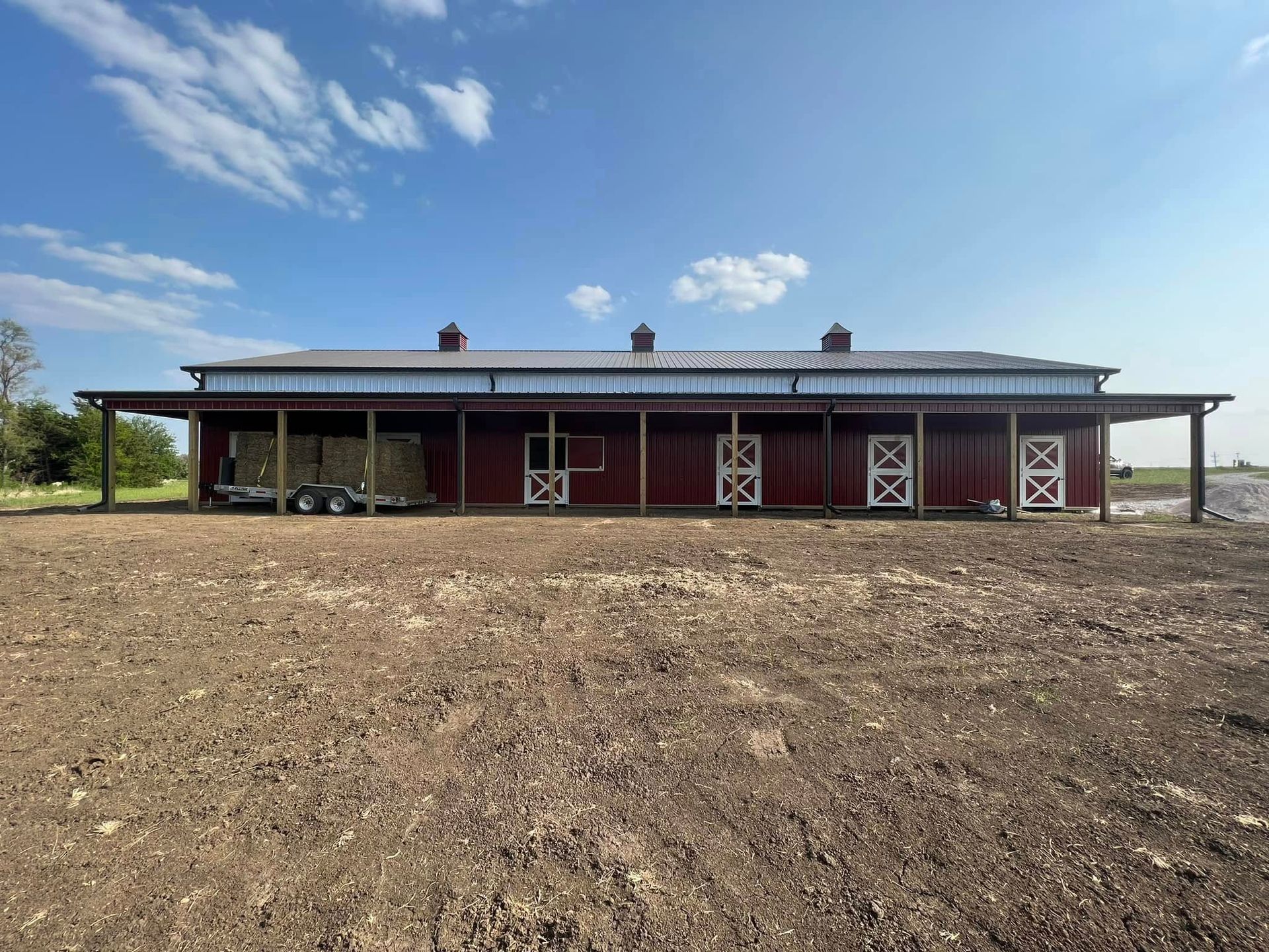 Red barn with a covered porch in a barren field under a blue sky with scattered clouds