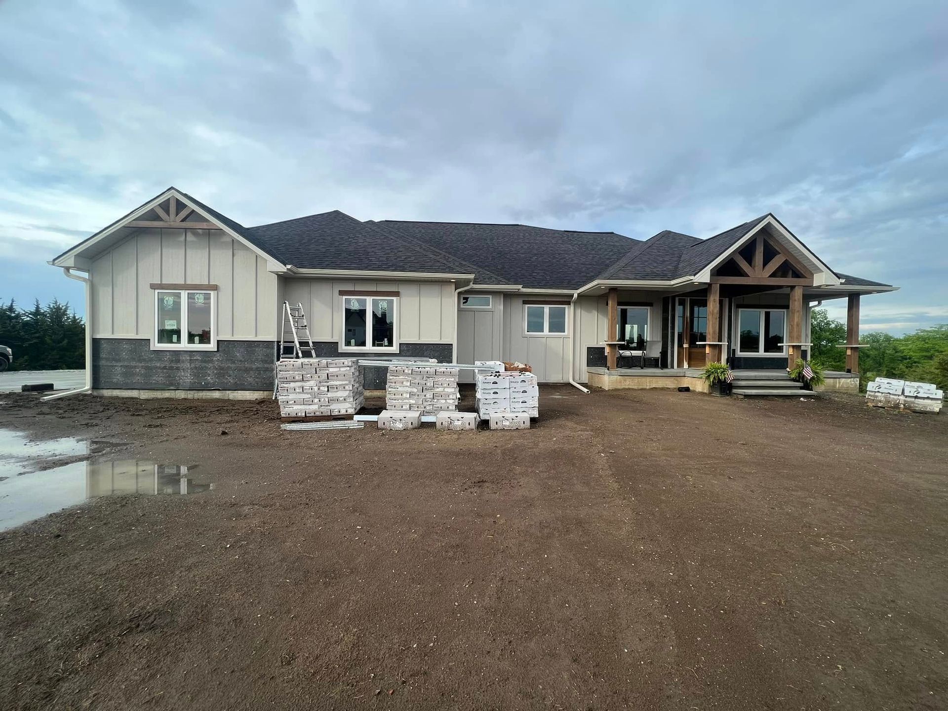 Single-story house under construction with stacked bricks in front and a muddy gravel driveway