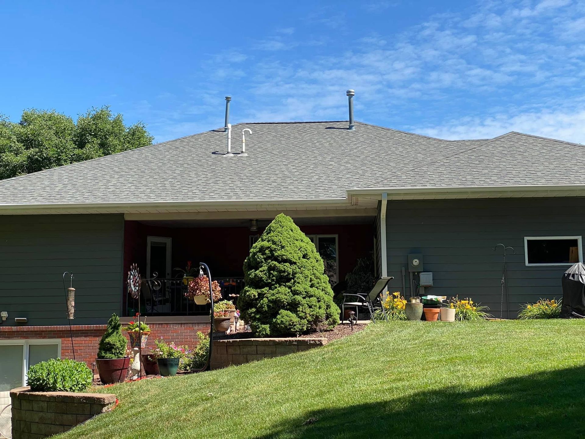 Single-story green house with a gray roof, front porch, and landscaped yard on a sunny day