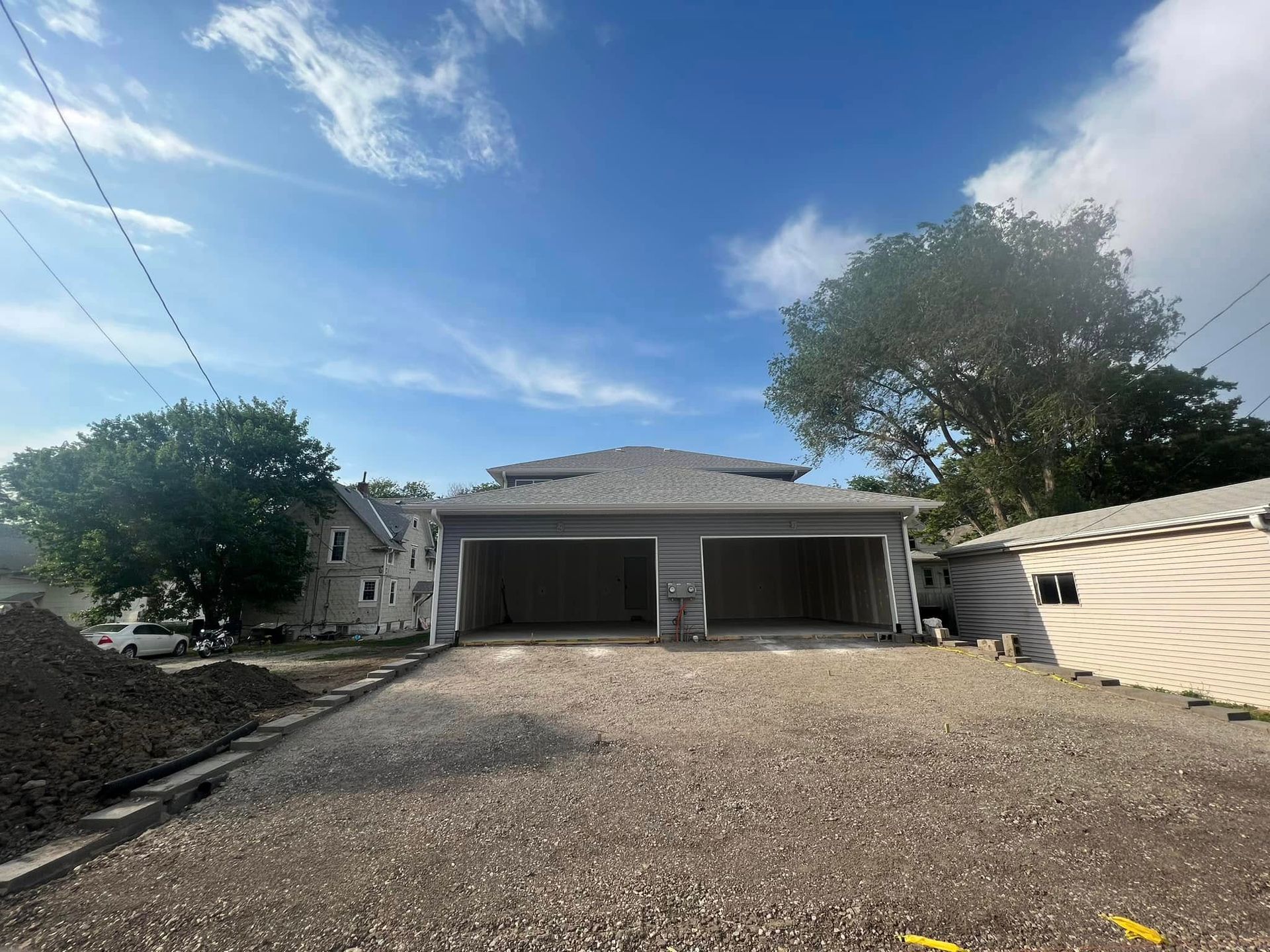 Gravel driveway leading to a gray two-car garage under a blue sky with trees nearby
