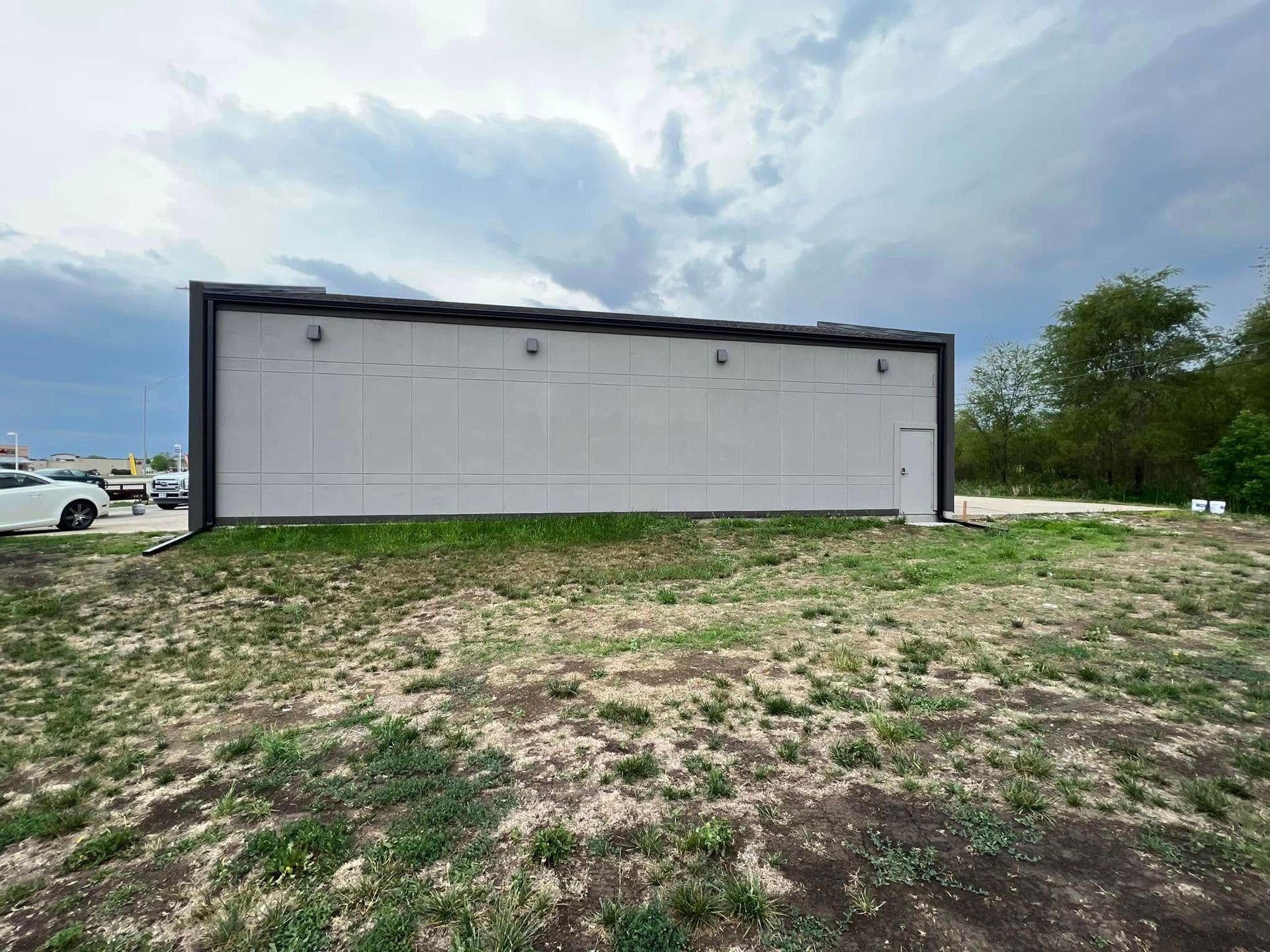 White industrial building on a grassy lot under a cloudy sky