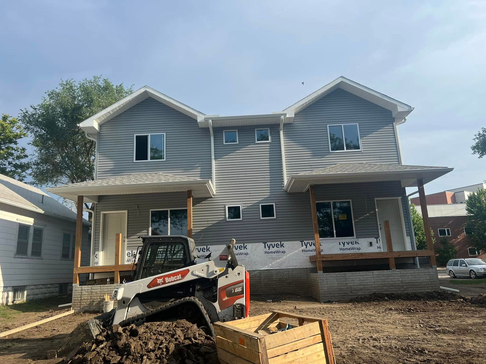 Two-story house under construction with a skid steer and gravel in front