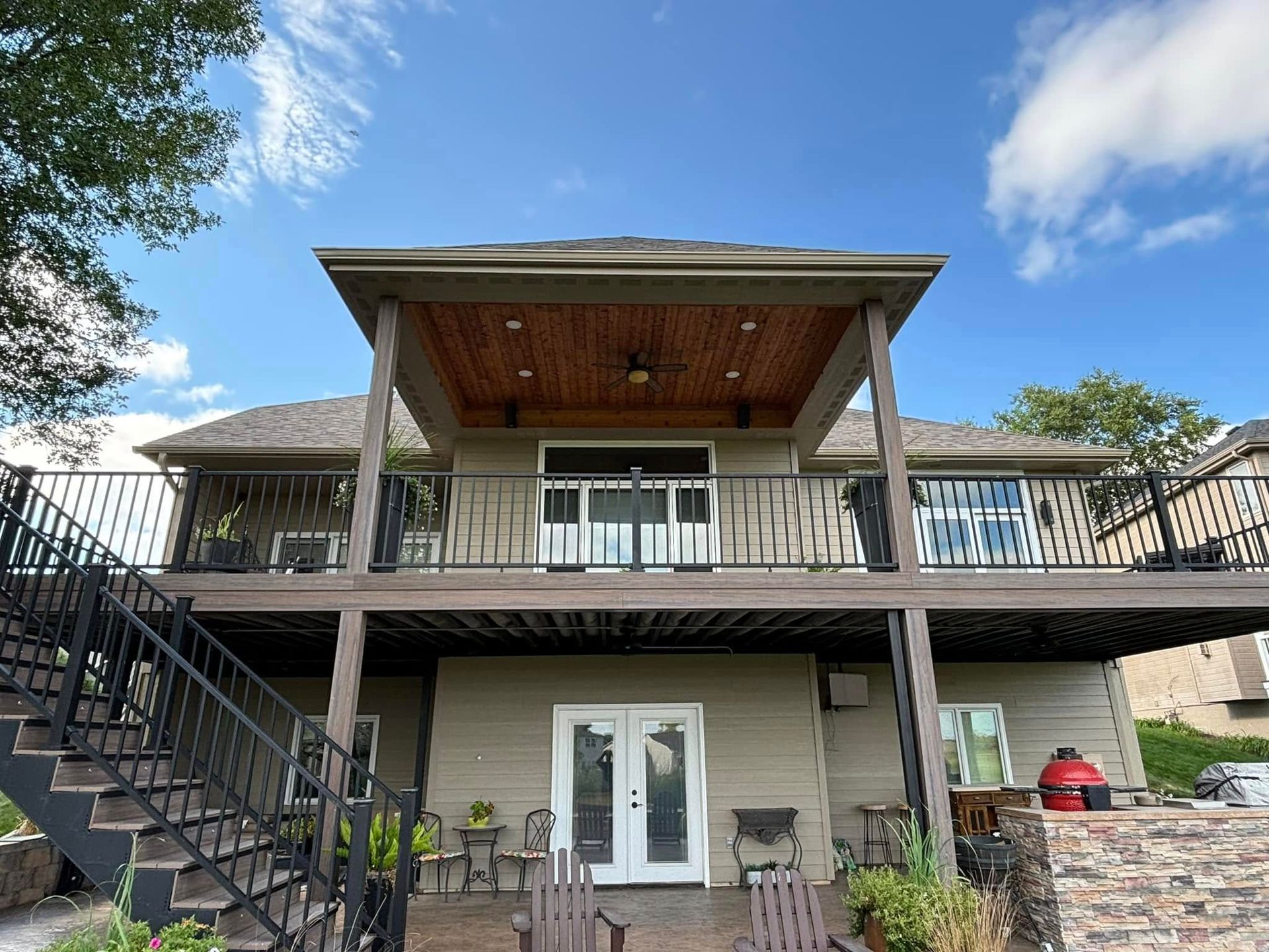 Two-story house with a wraparound deck, exterior stairs, and a car parked beneath it under a blue sky