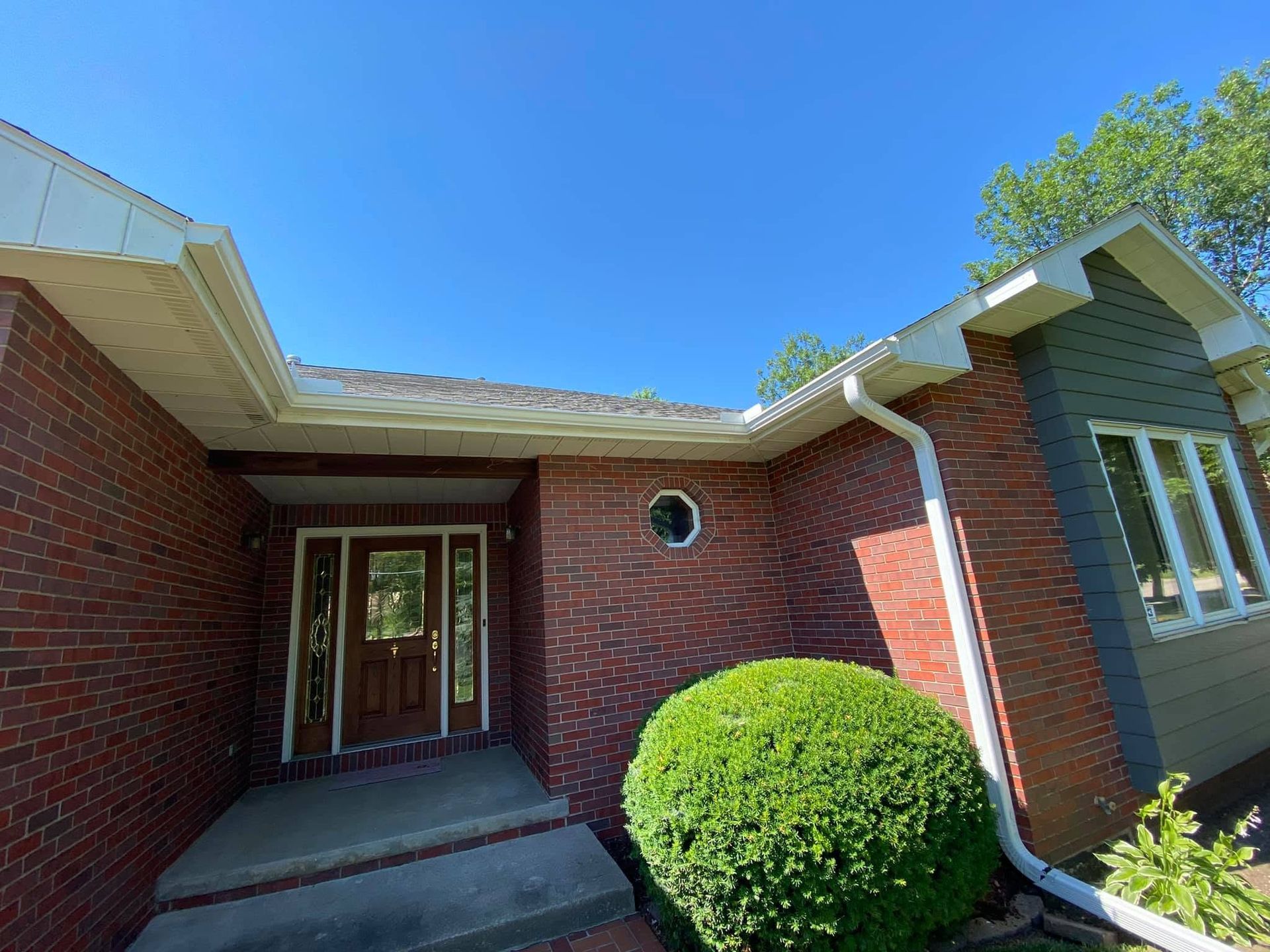 Brick house front entry with covered porch, white gutters, and a round green shrub.