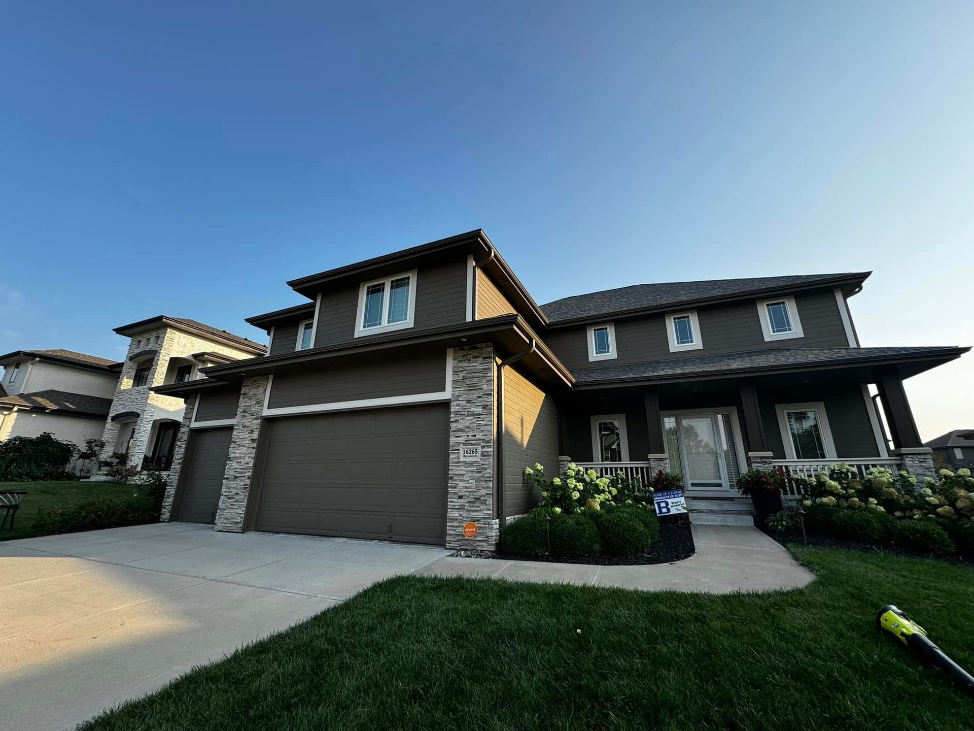 Two-story suburban house with a double garage, stone accents, and a front lawn at dusk