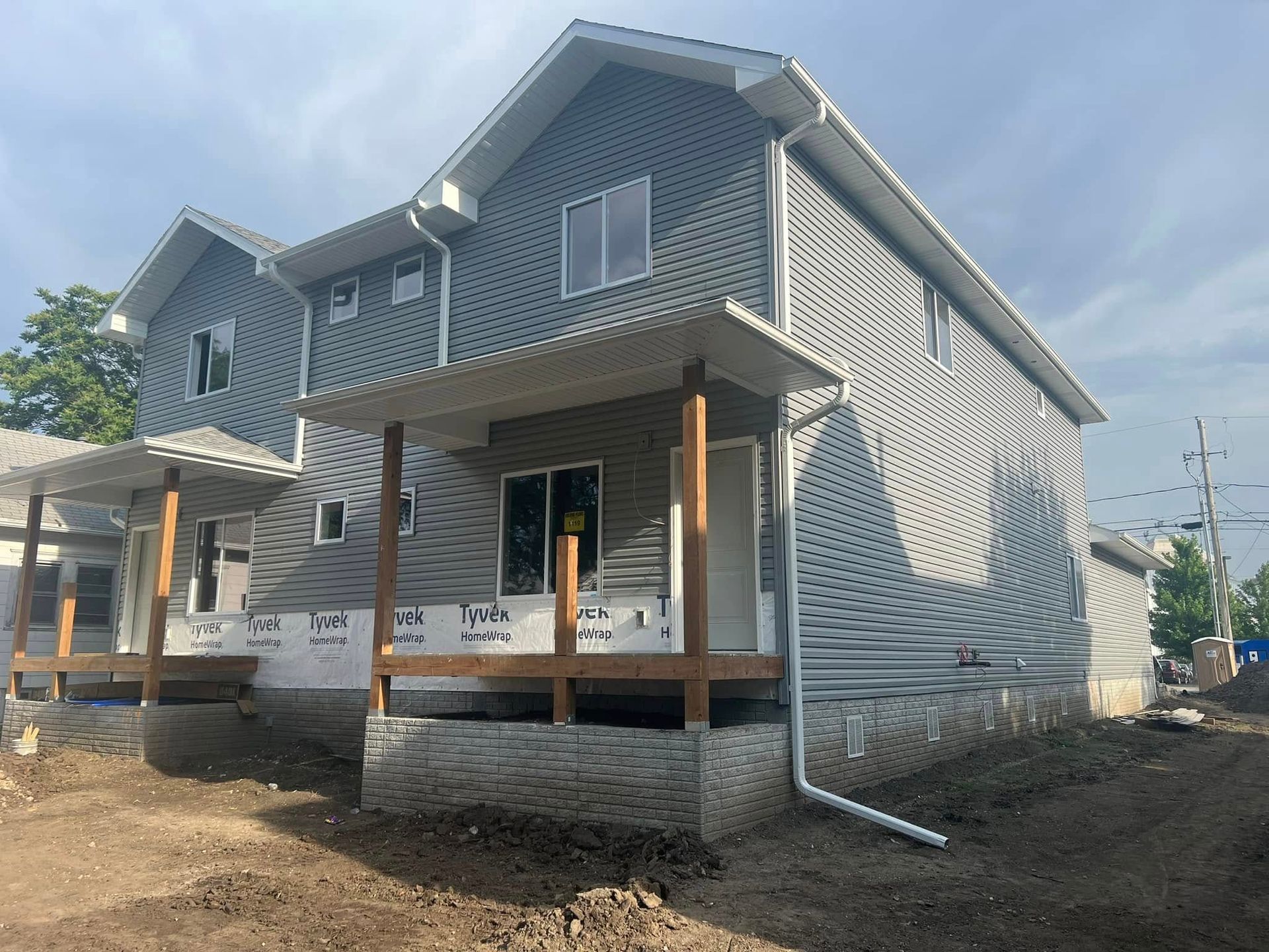 Partially built two-story house with gray siding and front porch on a dirt lot