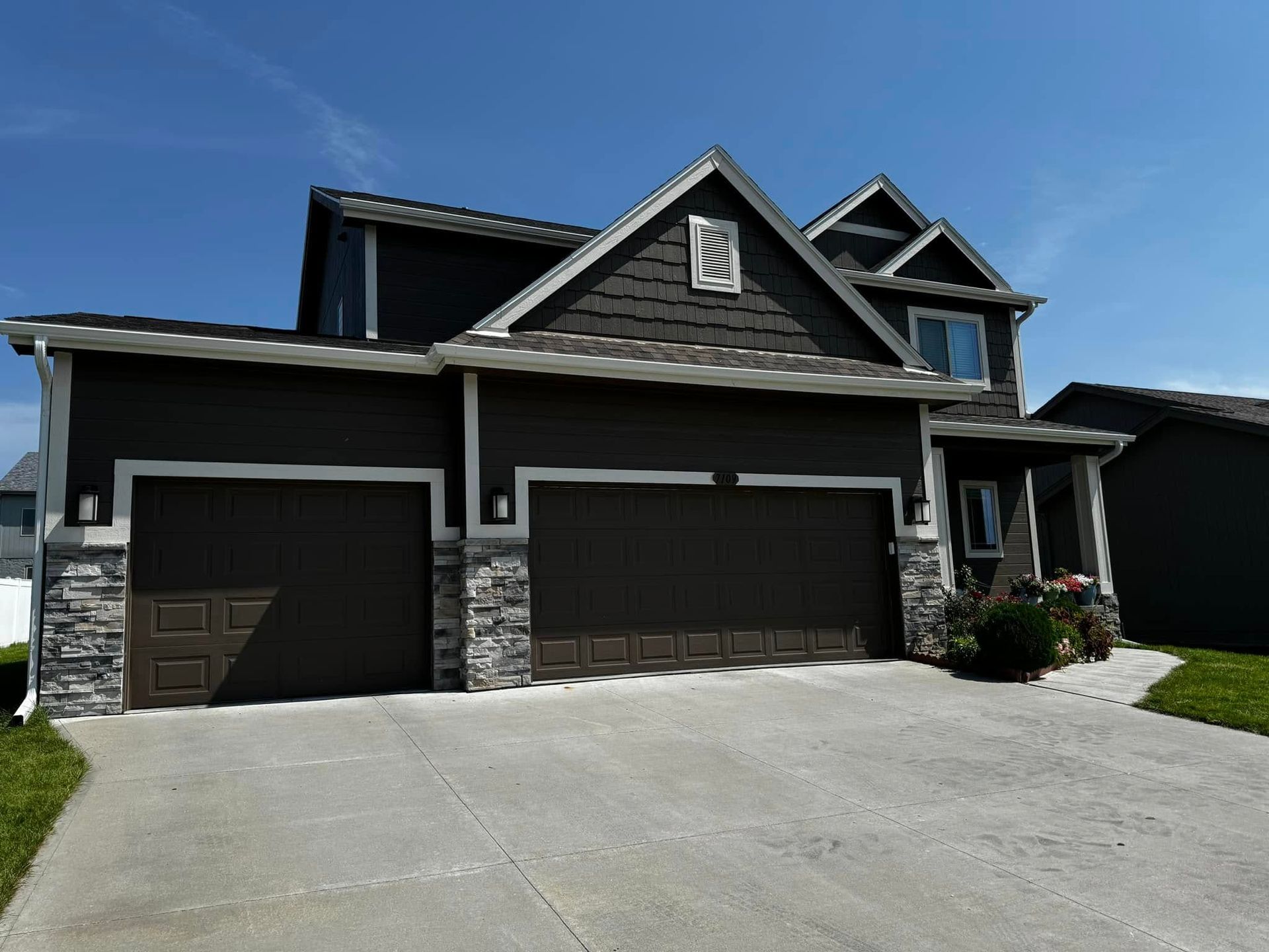 Modern two-story house with dark siding, stone accents, and a three-car garage under a clear blue sky
