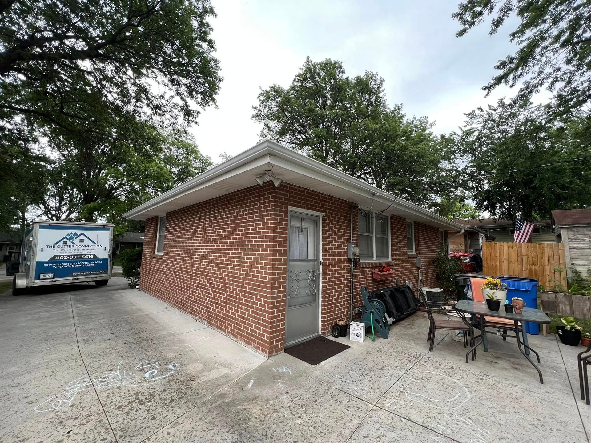 Brick garage with metal door, gravel driveway, and outdoor chairs beside a fenced yard.