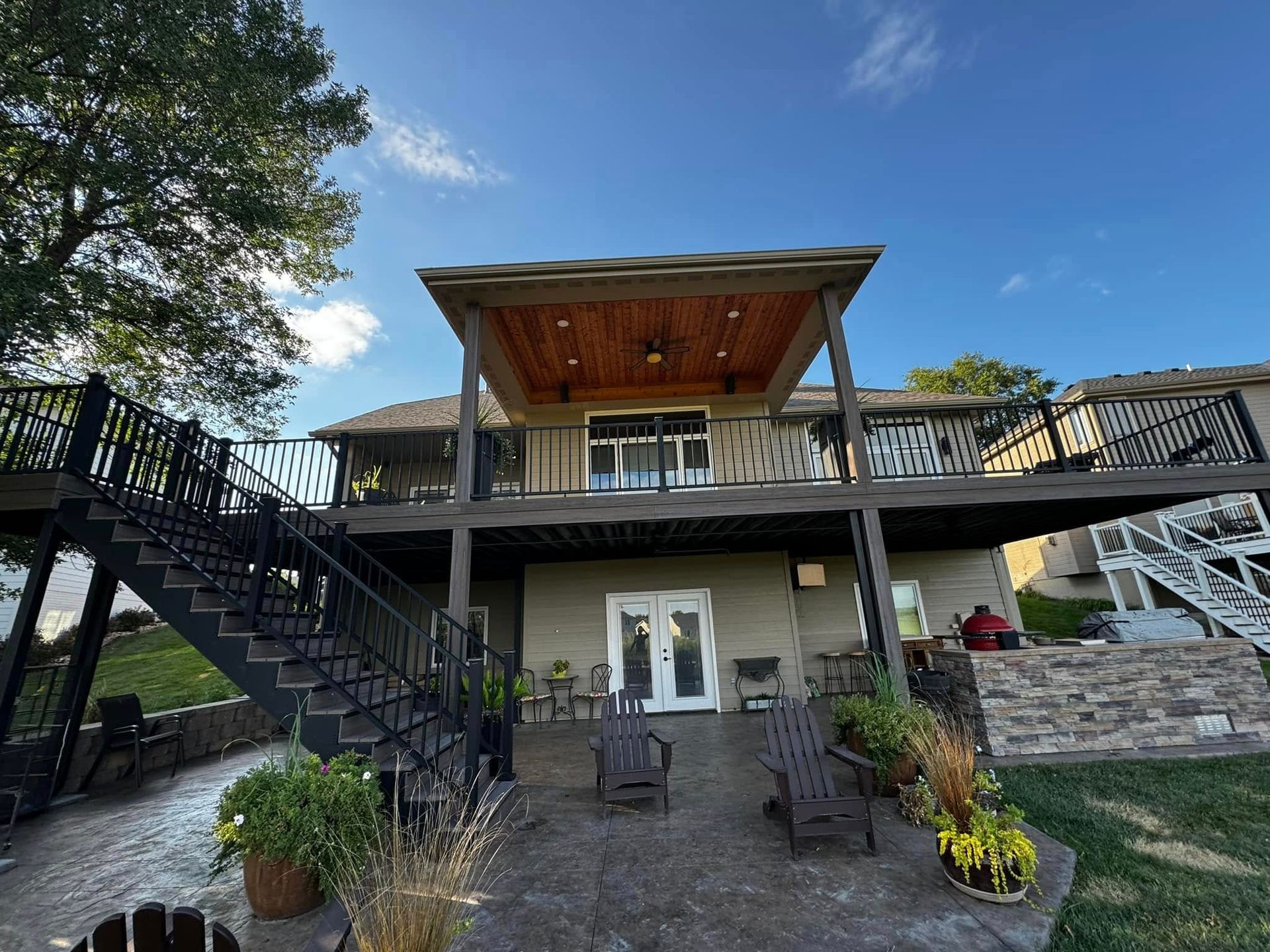 Modern two-story house with a large deck, exterior stairs, and stone landscaping under a blue sky