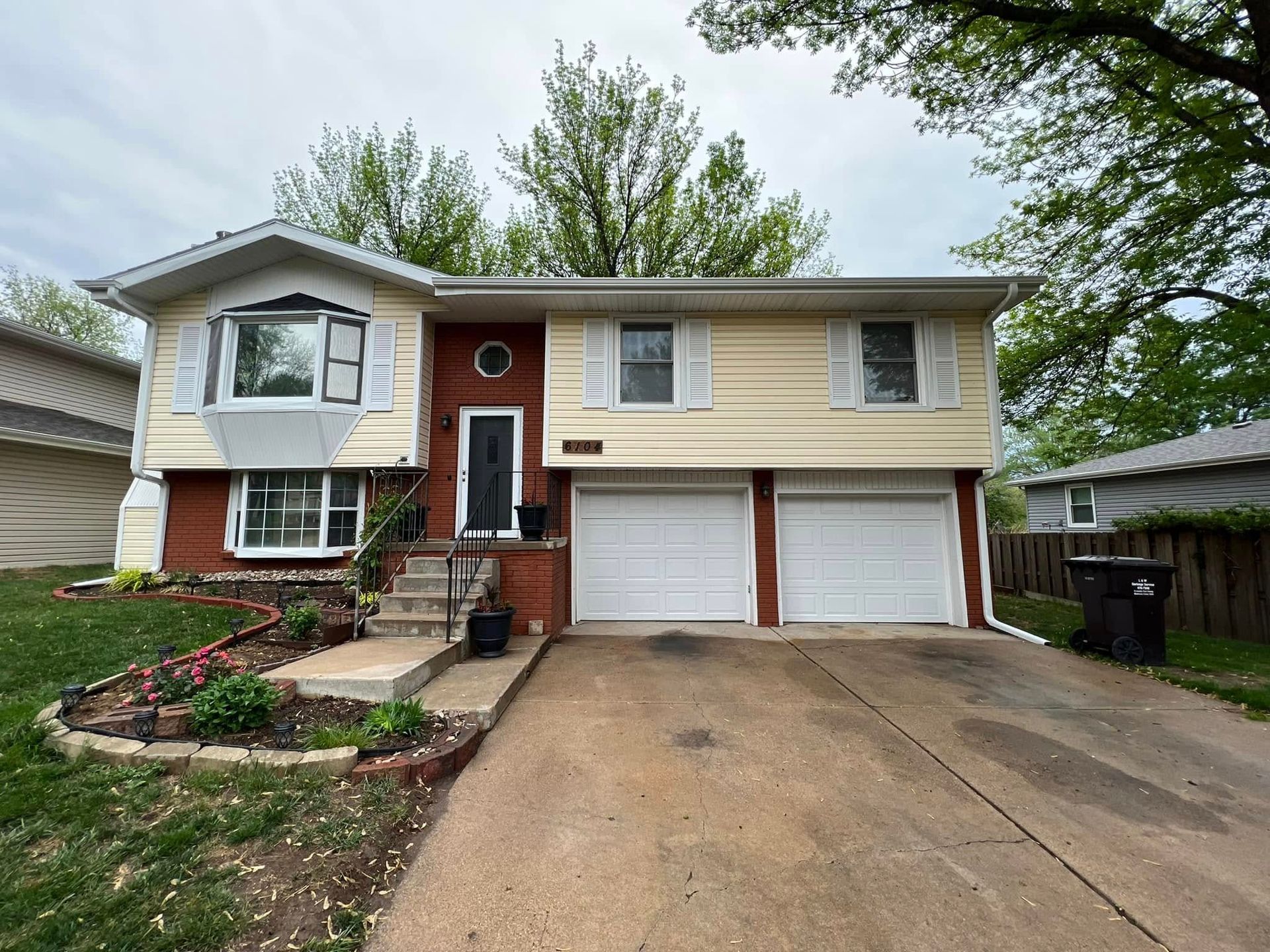 Two-story beige house with red front door, double garage, and wide driveway