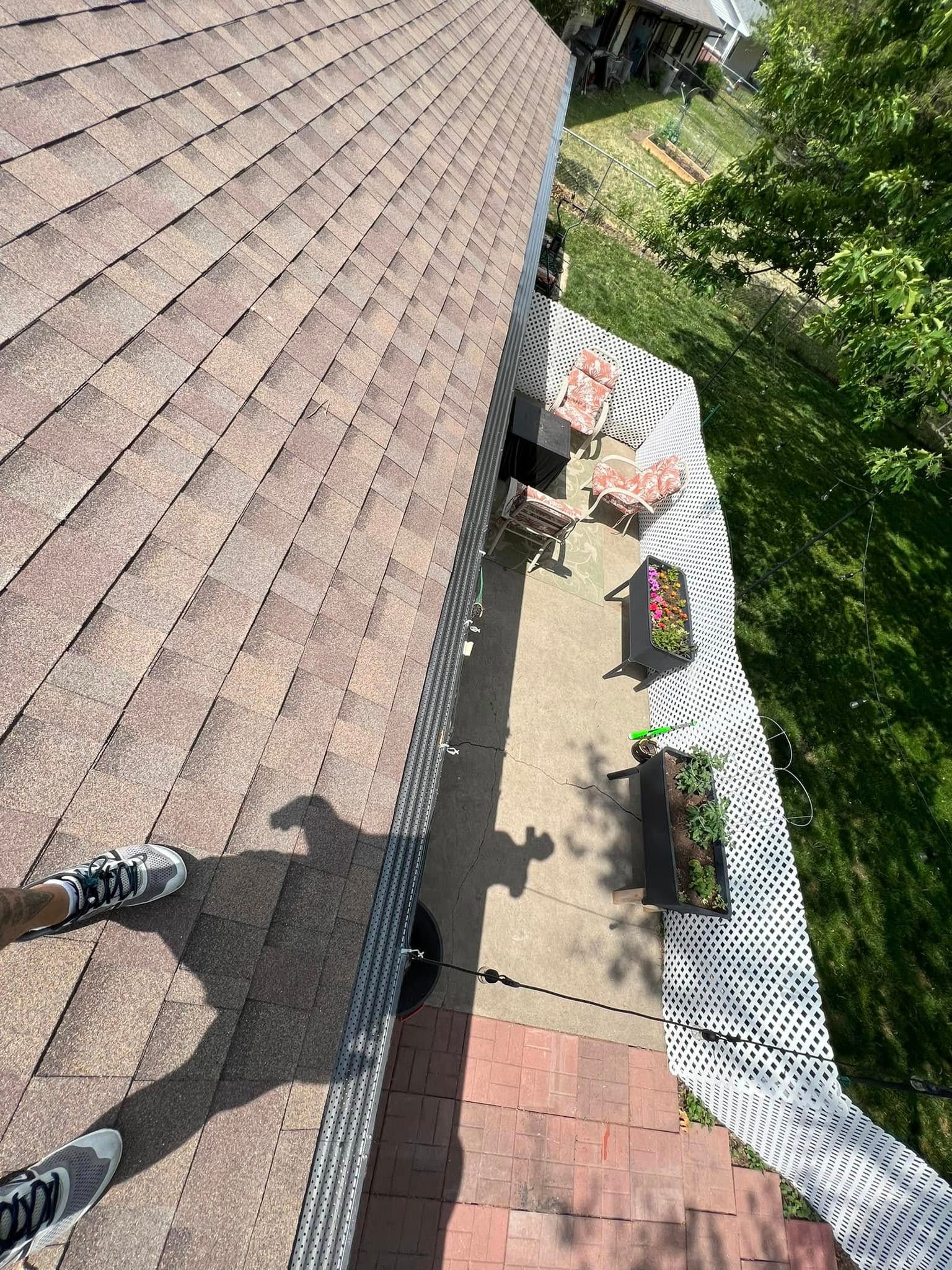 Rooftop view of a yard with garden beds, trees, and a person’s foot at the edge of the roof