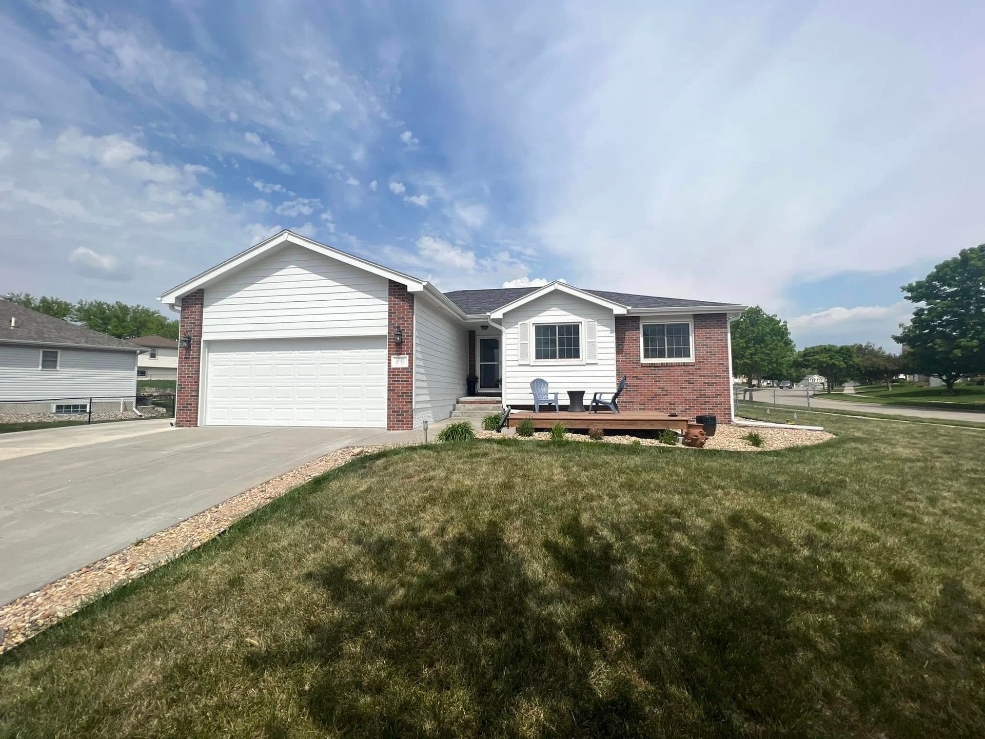 Single-story brick house with attached garage, driveway, and front lawn under a cloudy sky