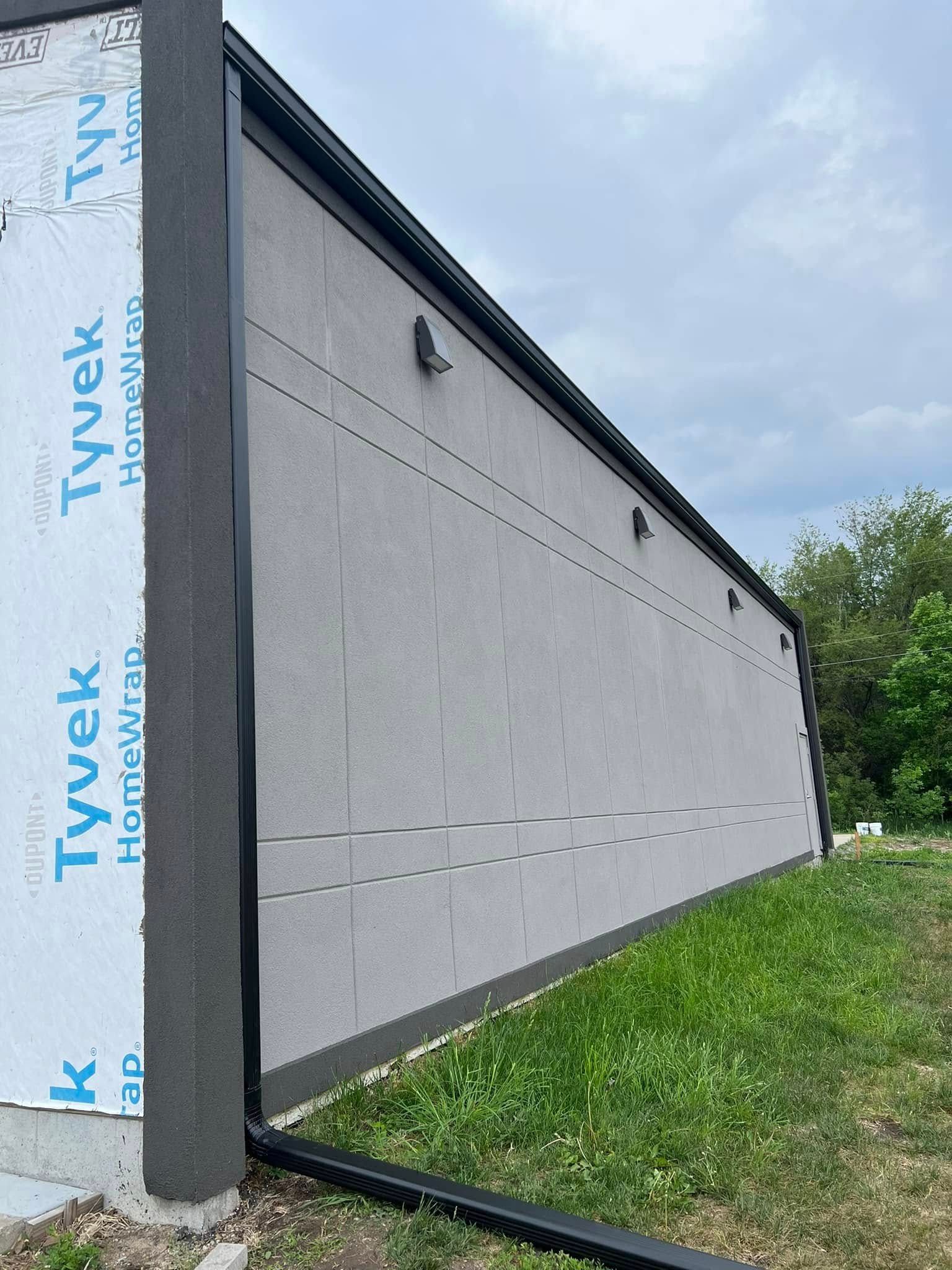 Side view of a gray house wall wrapped in Tyvek underlayment beside grass and cloudy sky