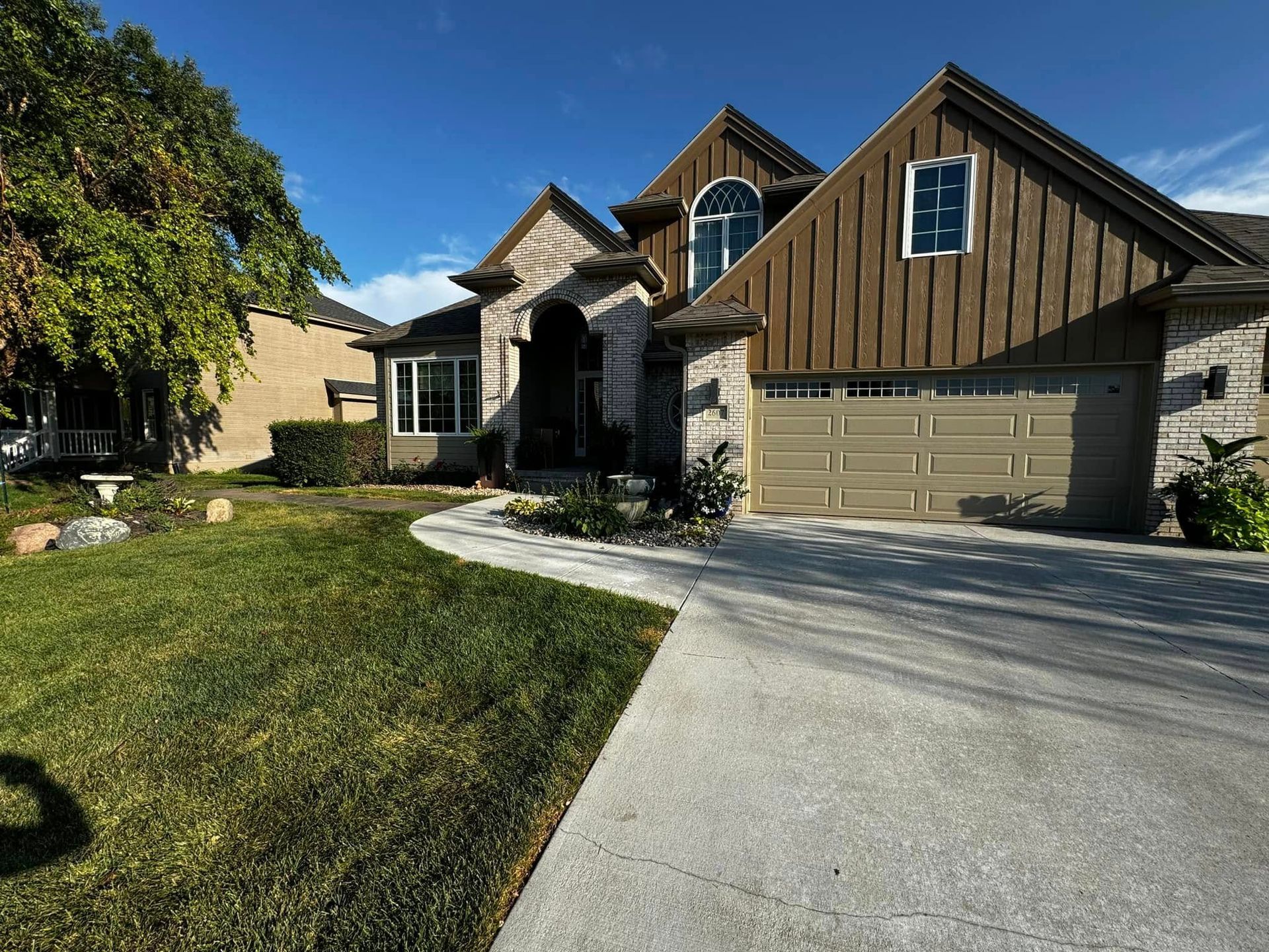 Suburban house with a two-car garage, curved driveway, and green front lawn in sunlight