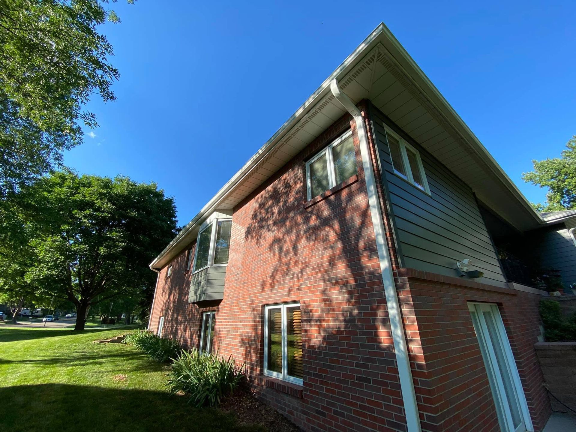Brick house with sloped roof and white siding on a grassy lawn under a bright blue sky