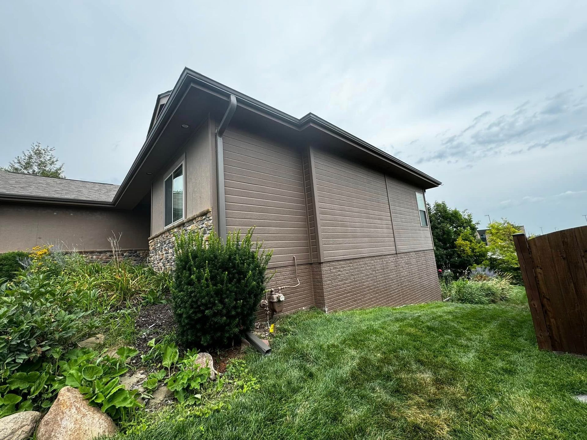 House exterior with beige siding and a steep roof, viewed from a grassy backyard garden.