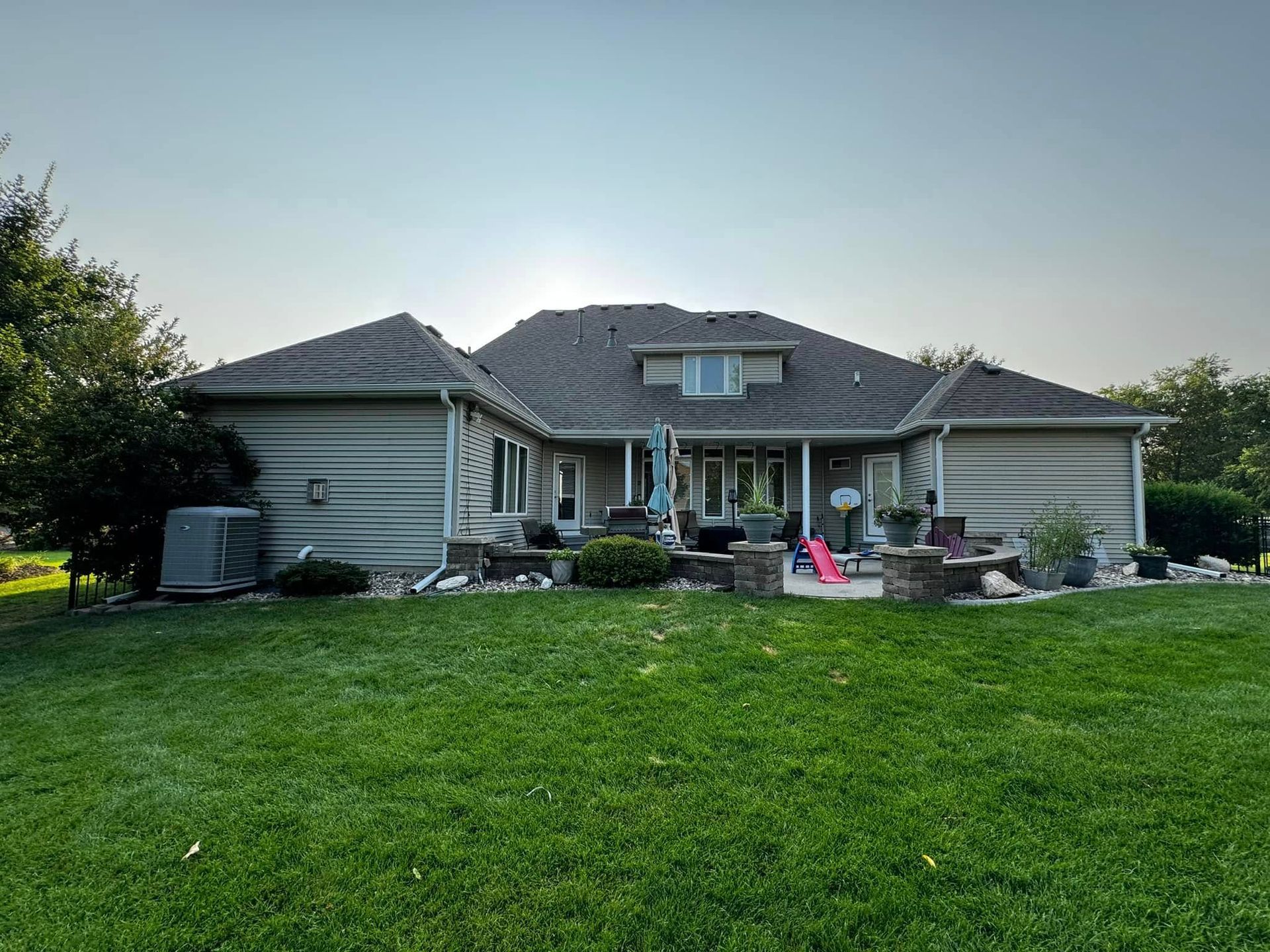 Suburban house with large green lawn, patio furniture, and a pink toy in the yard at dusk