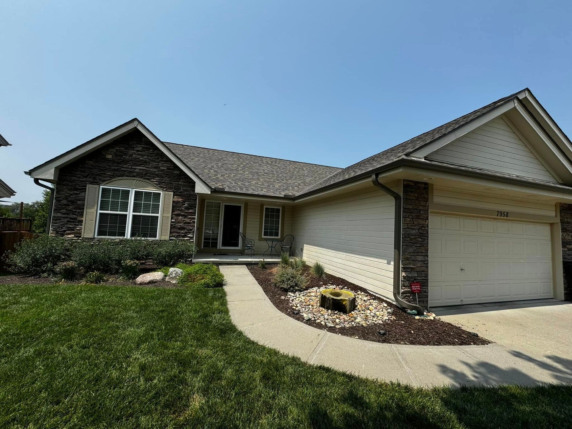 Suburban house with brick and siding, front lawn, curved walkway, and attached garage under a blue sky