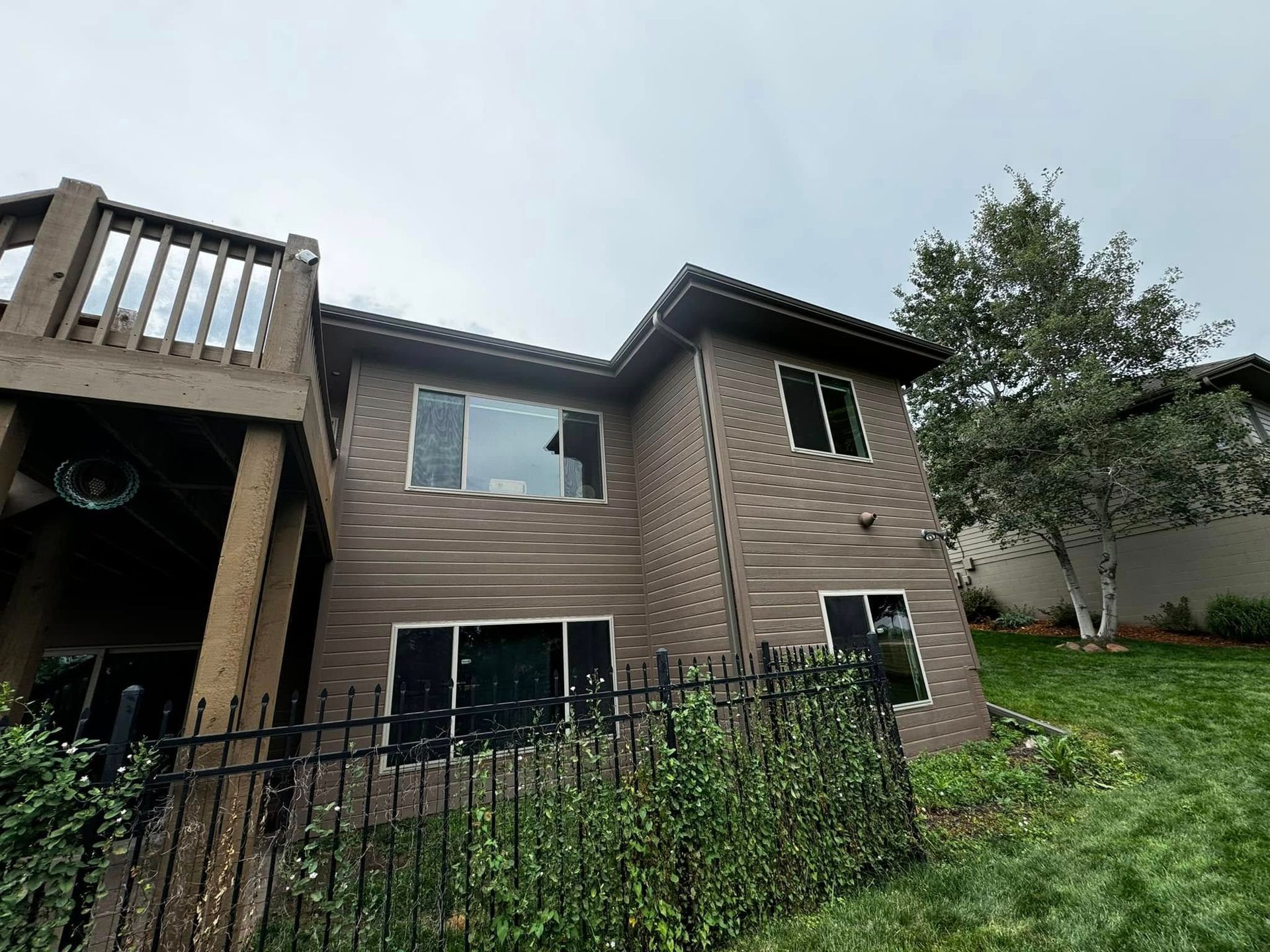Two-story brown house with black railings and a grassy sloped yard beside it