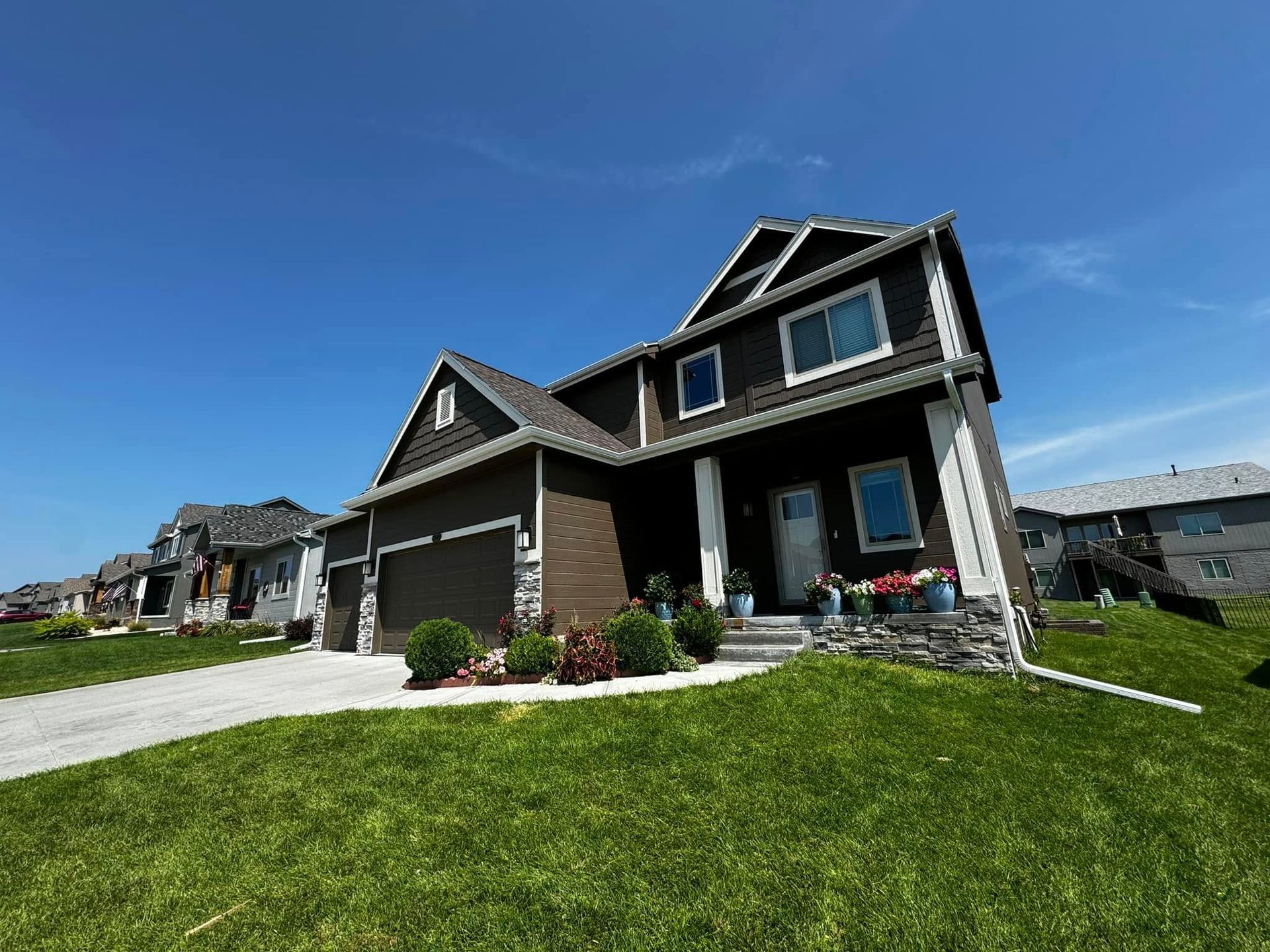 Suburban house with dark siding, garage, and bright green lawn under a blue sky