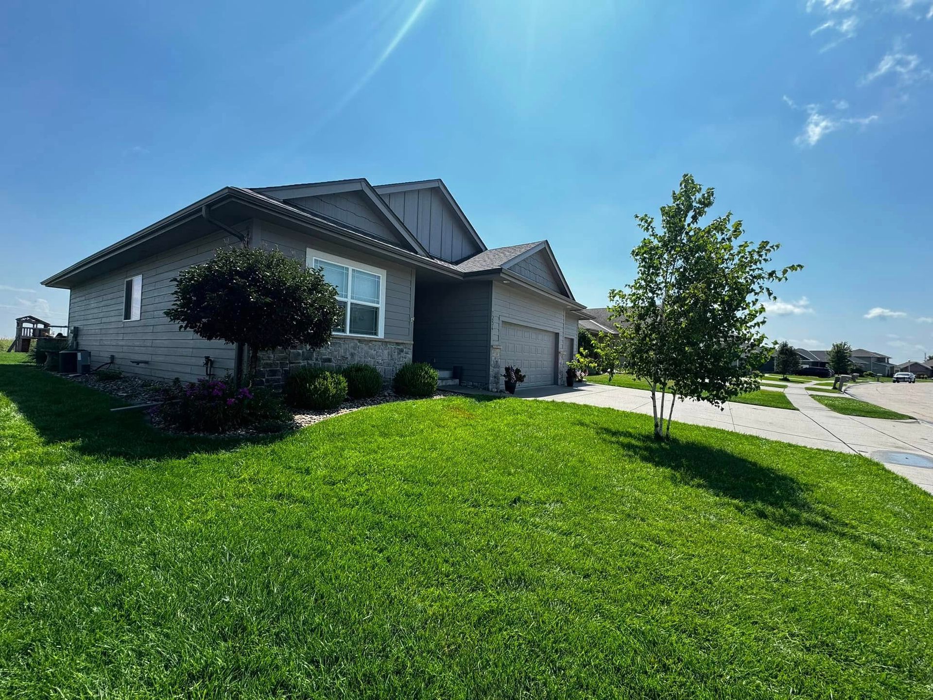Suburban house with a green lawn, tree, and driveway under a bright blue sky