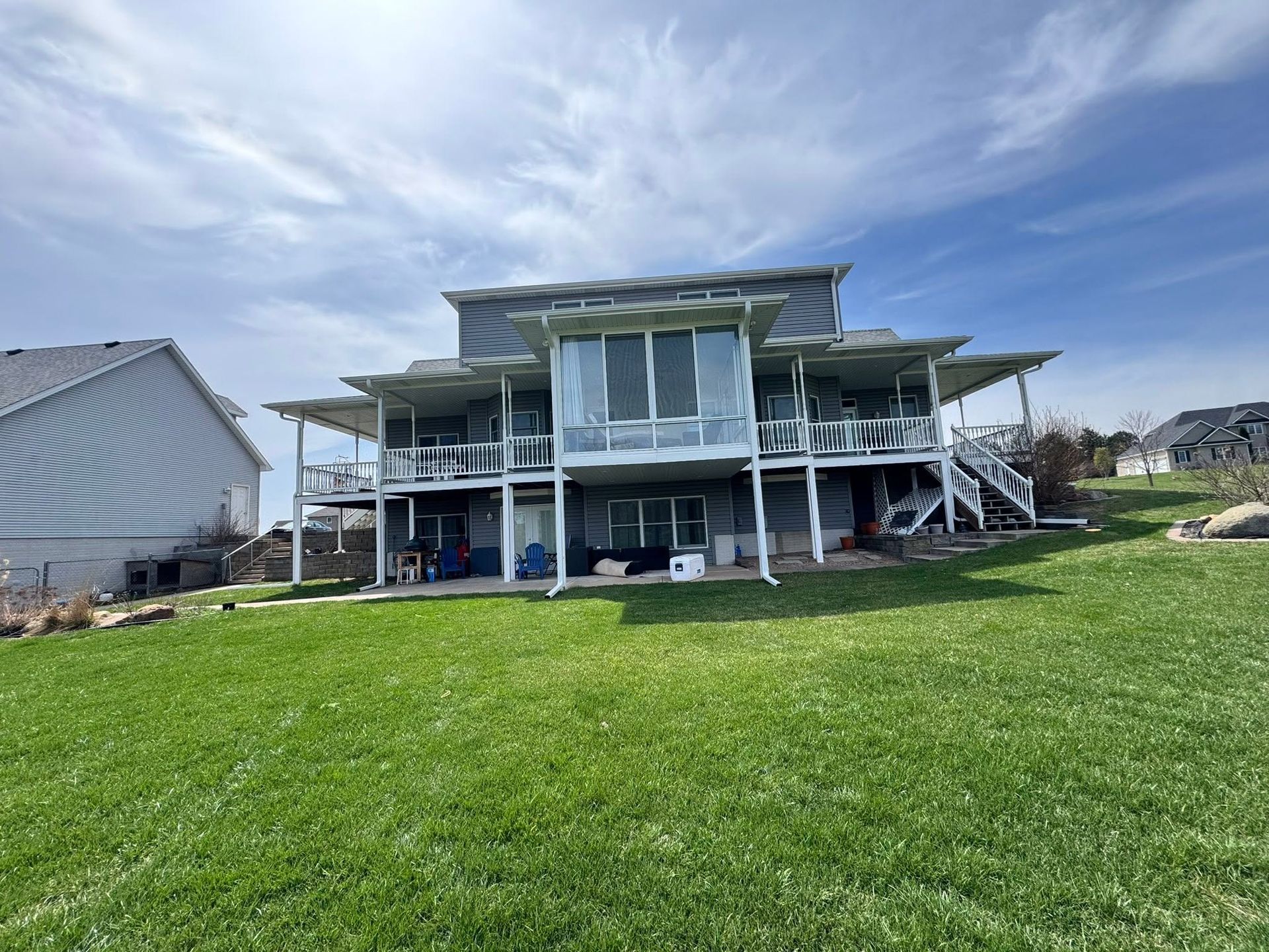 Two-story beach house with raised deck and blue sky over a green lawn