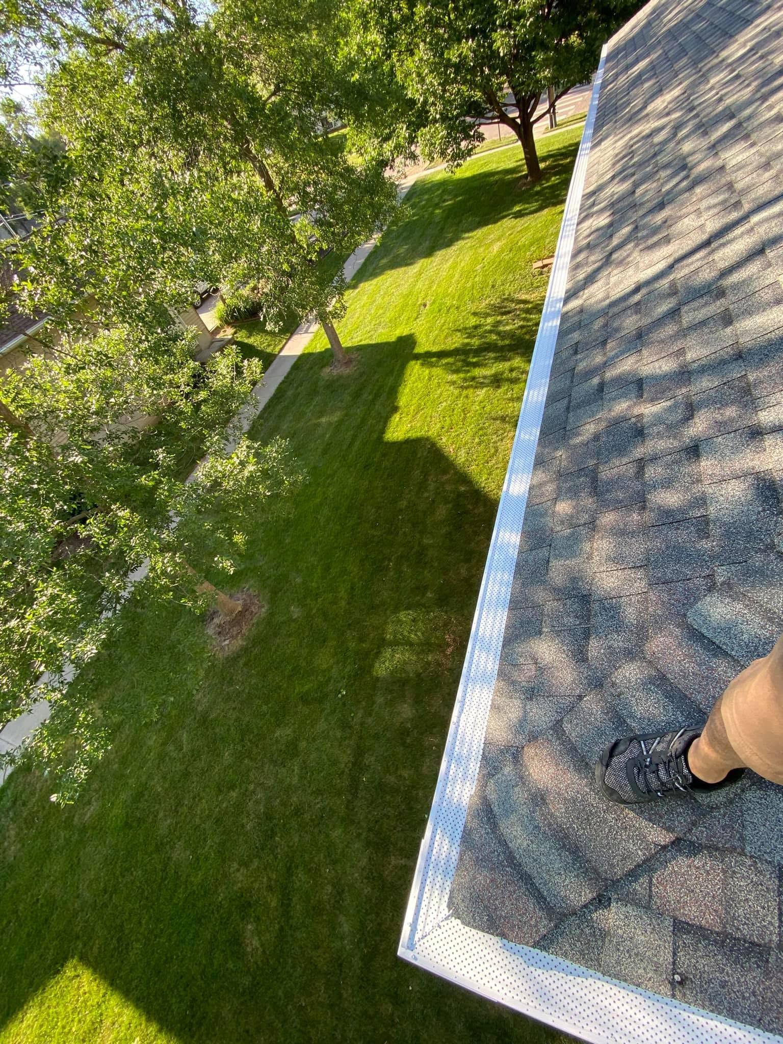 Person standing on a roof beside trees and a green lawn below