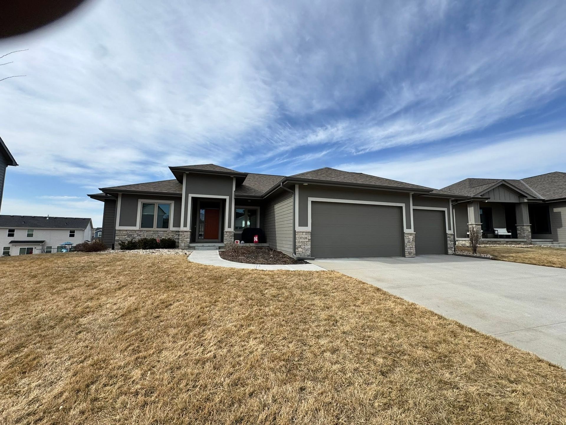Single-story suburban house with stone facade, gray garage, and a dry front lawn under a blue sky.