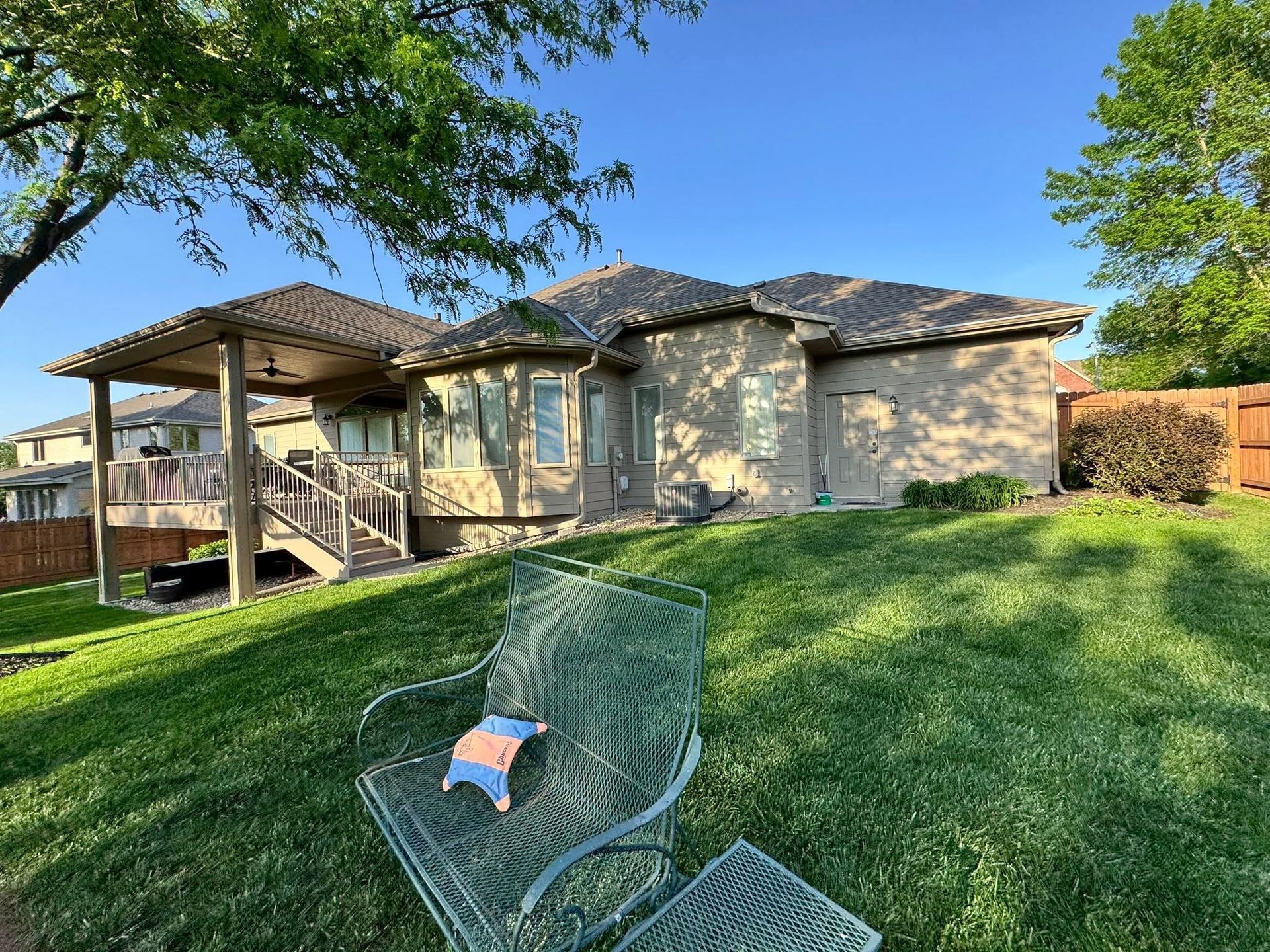 Backyard patio with covered deck, grassy lawn, and a green chair in the foreground.