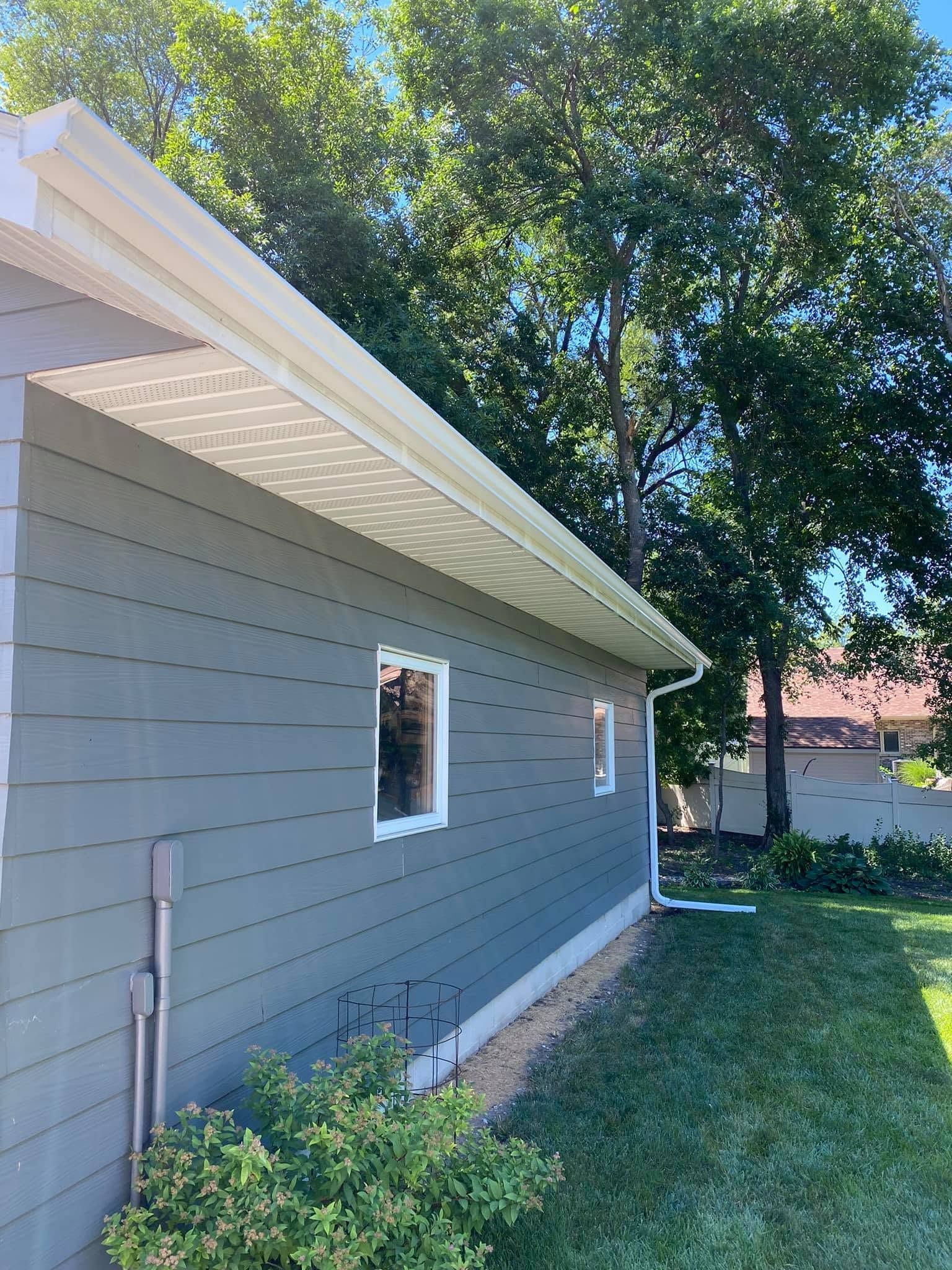 Side of a gray house with white eaves, a small window, and a grassy yard with trees.