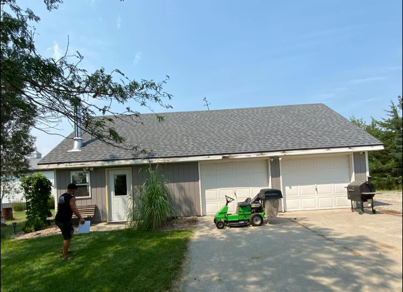 Suburban house with two garage doors, a green mower on the driveway, and a person standing by the front porch.