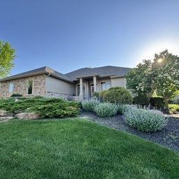 Single-story suburban house with manicured lawn, landscaped shrubs, and a bright blue sky