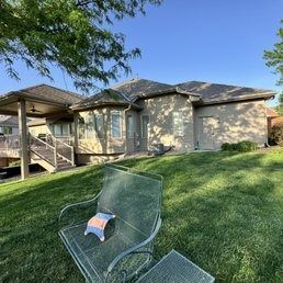 Backyard with a house, covered porch, and a chair on a green lawn in sunlight