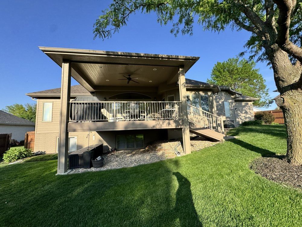 Backyard patio with covered deck, stairs, and green lawn beside a brick house
