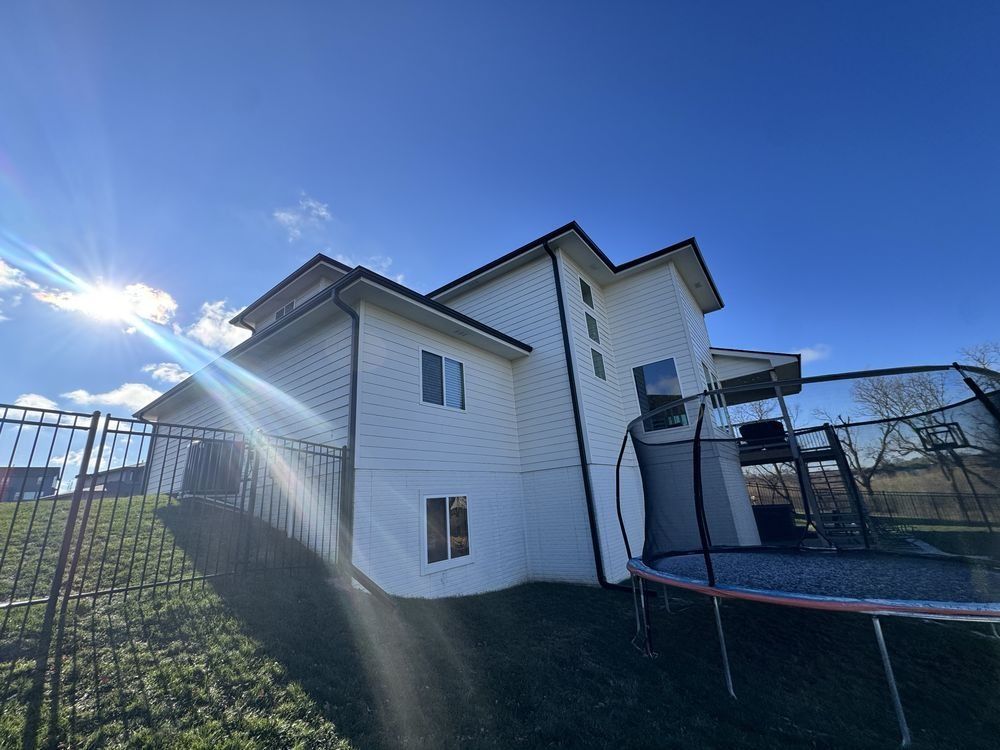 White house exterior with fence, sun flare, and trampoline in a backyard under a blue sky
