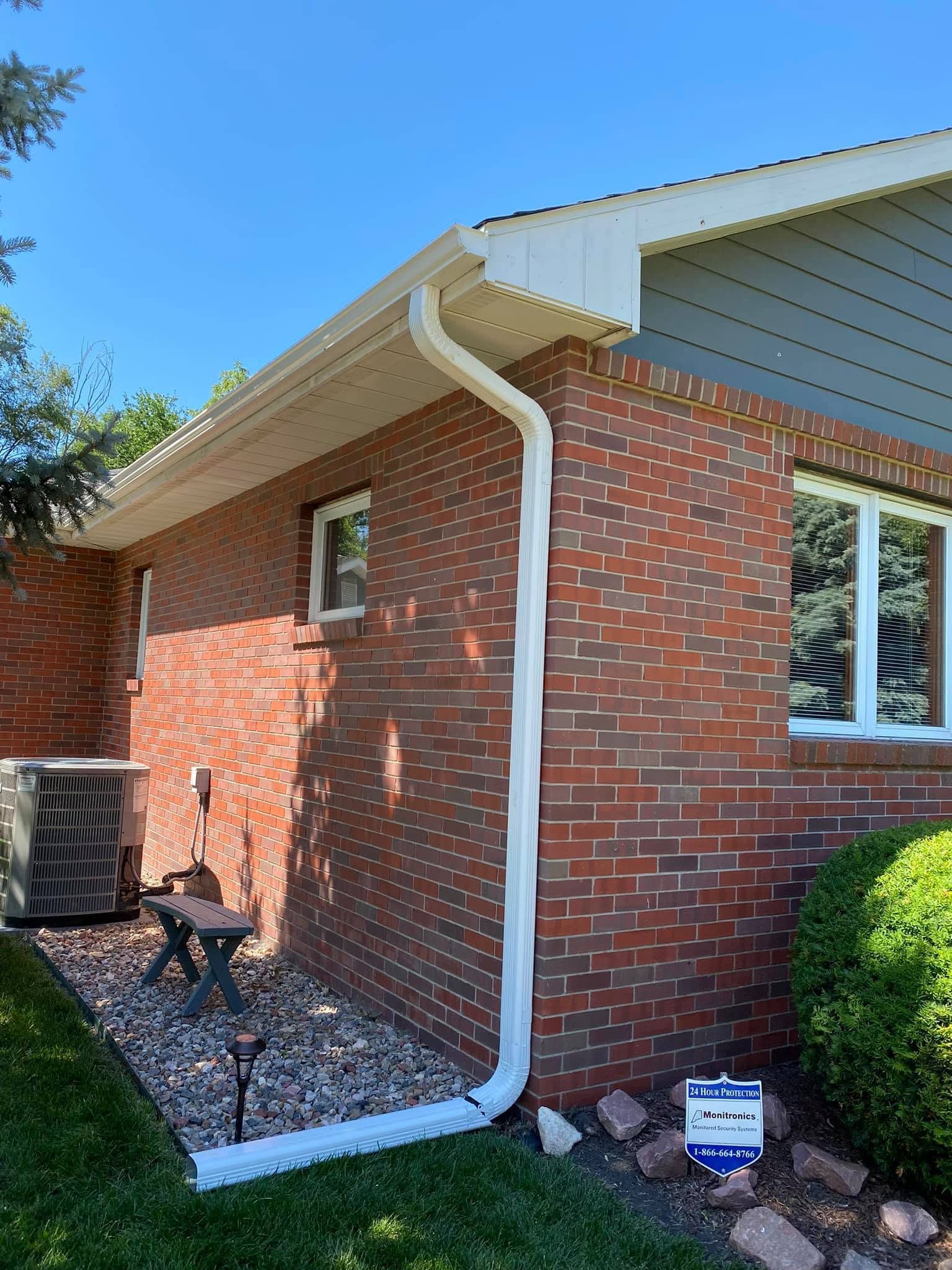 Brick house exterior with white gutters, a side window, and landscaped shrubs under a blue sky