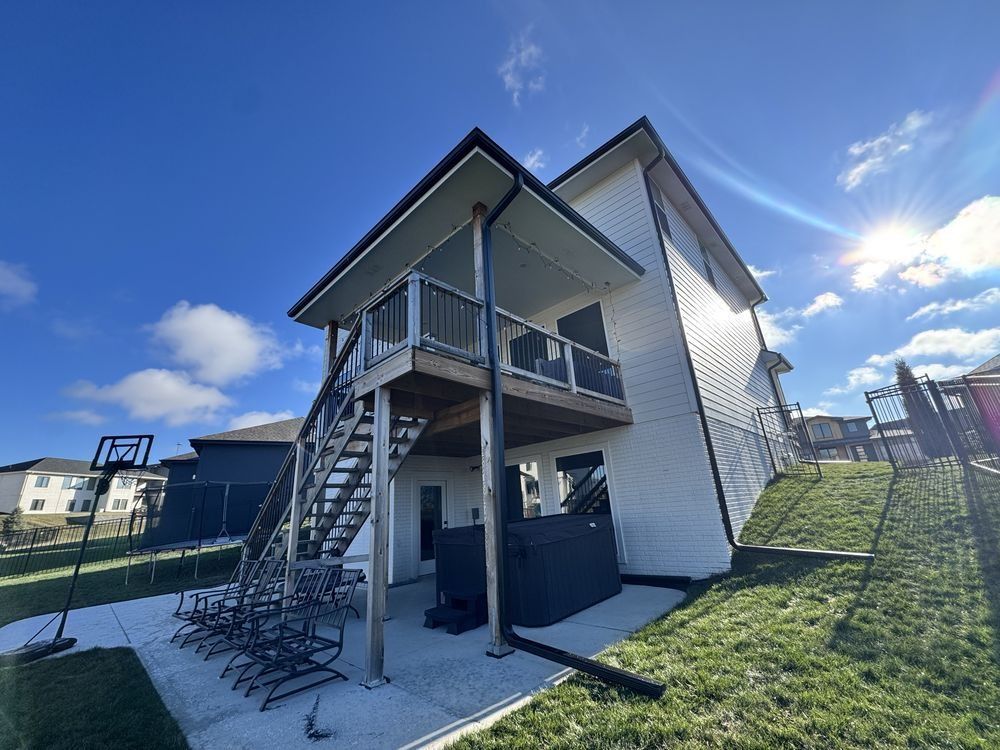 Exterior view of a two-story apartment building with metal stairs and a grassy yard under a blue sky